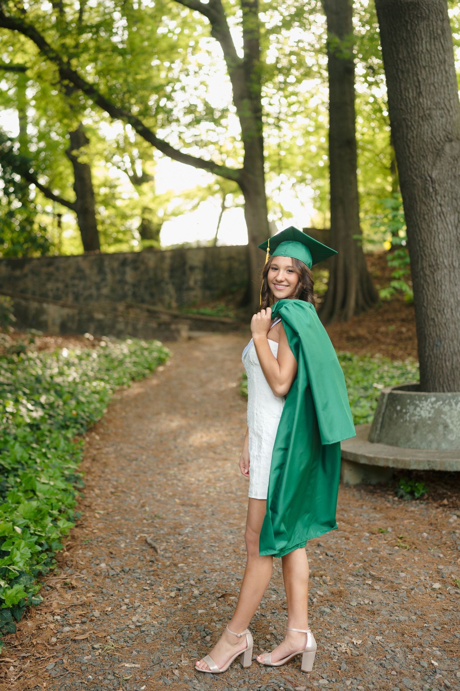 High school senior girl with cap and gown over her shoulder at the Raleigh Rose Garden in Raleigh, North Carolina.