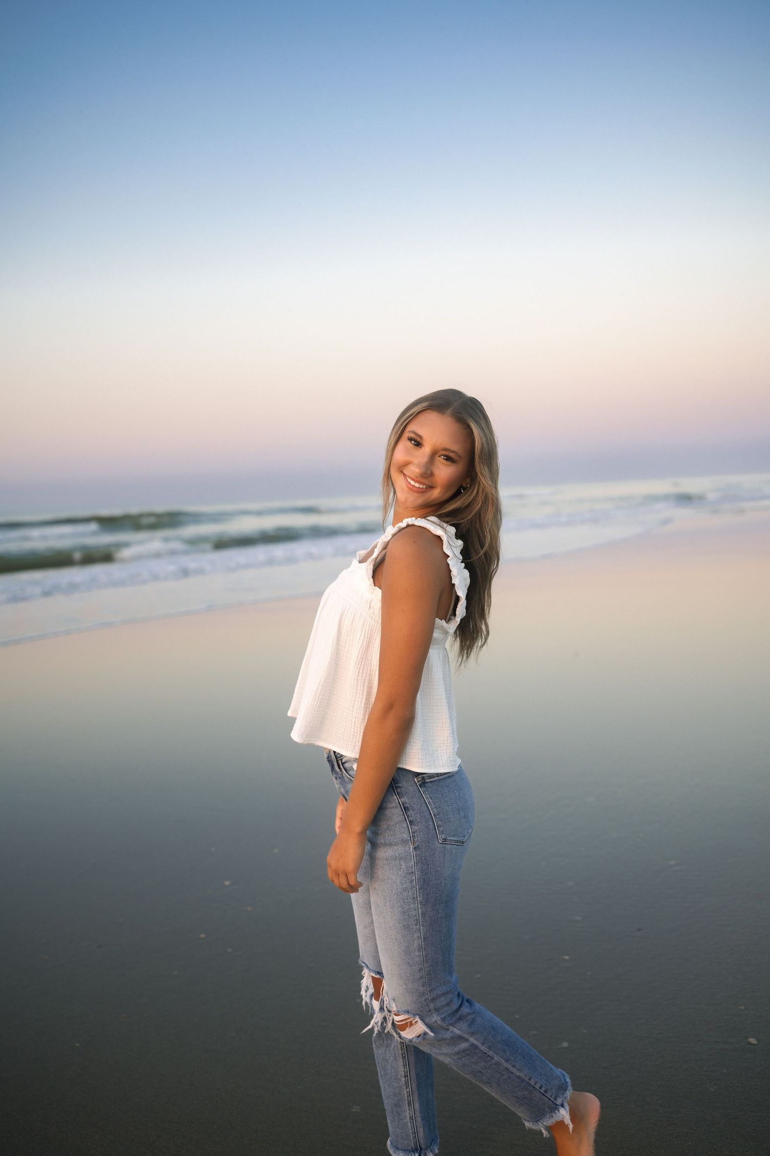 Sunrise senior portrait at Folly Beach with simple white tank and denim outfit.