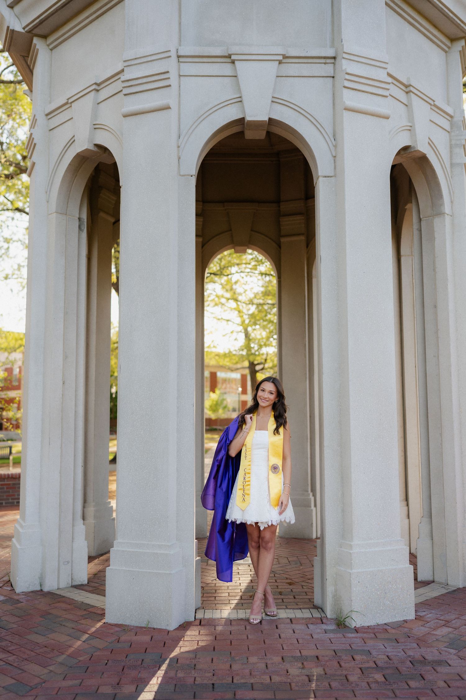 College graduate in cap and gown posing at the Cupola on East Carolina University campus in Greenville, NC