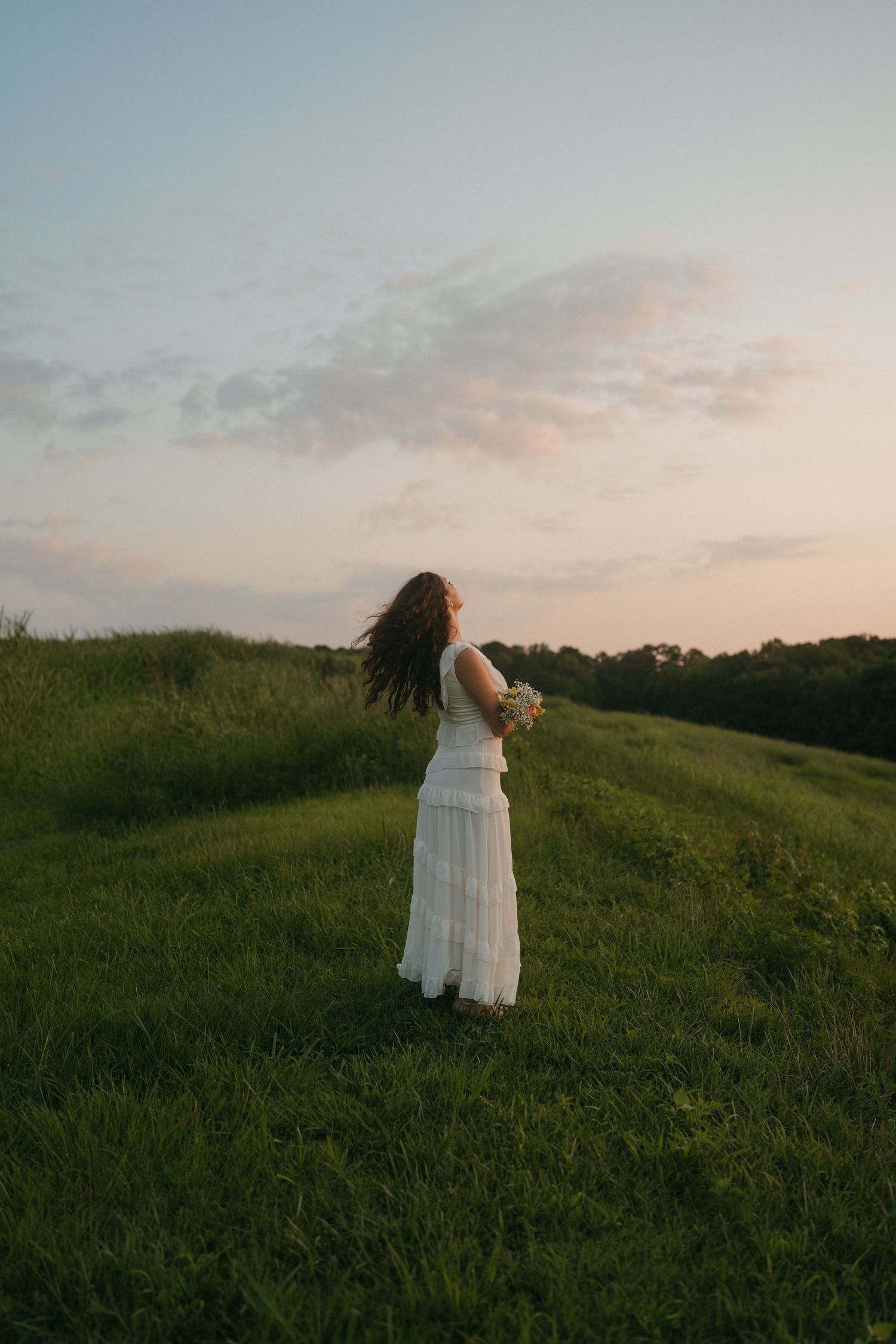 Senior girl in a white dress holding flowers in a field in Raleigh, North Carolina