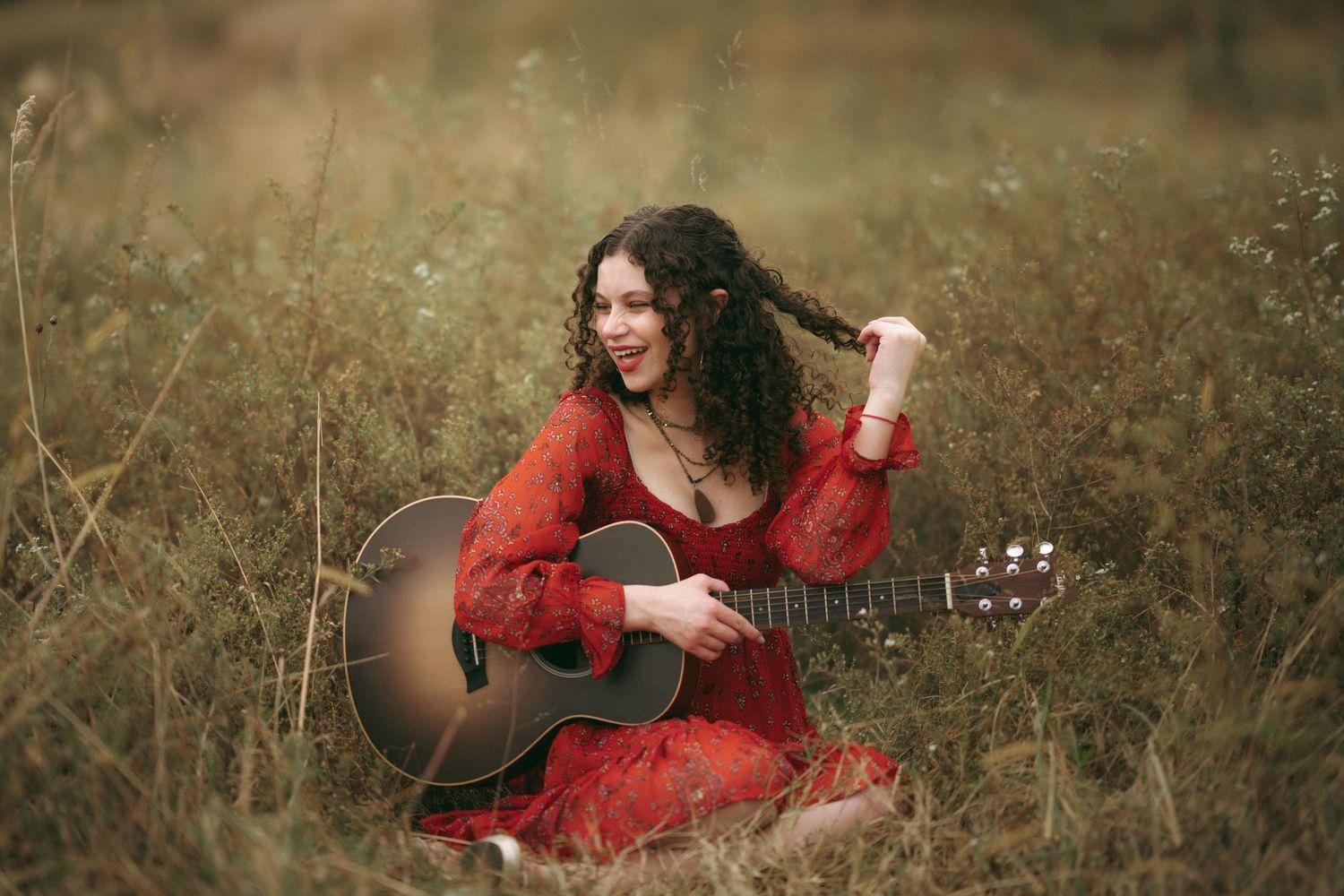High school senior girl holding a guitar and playing with her hair at the North Carolina Museum of Art in Raleigh.