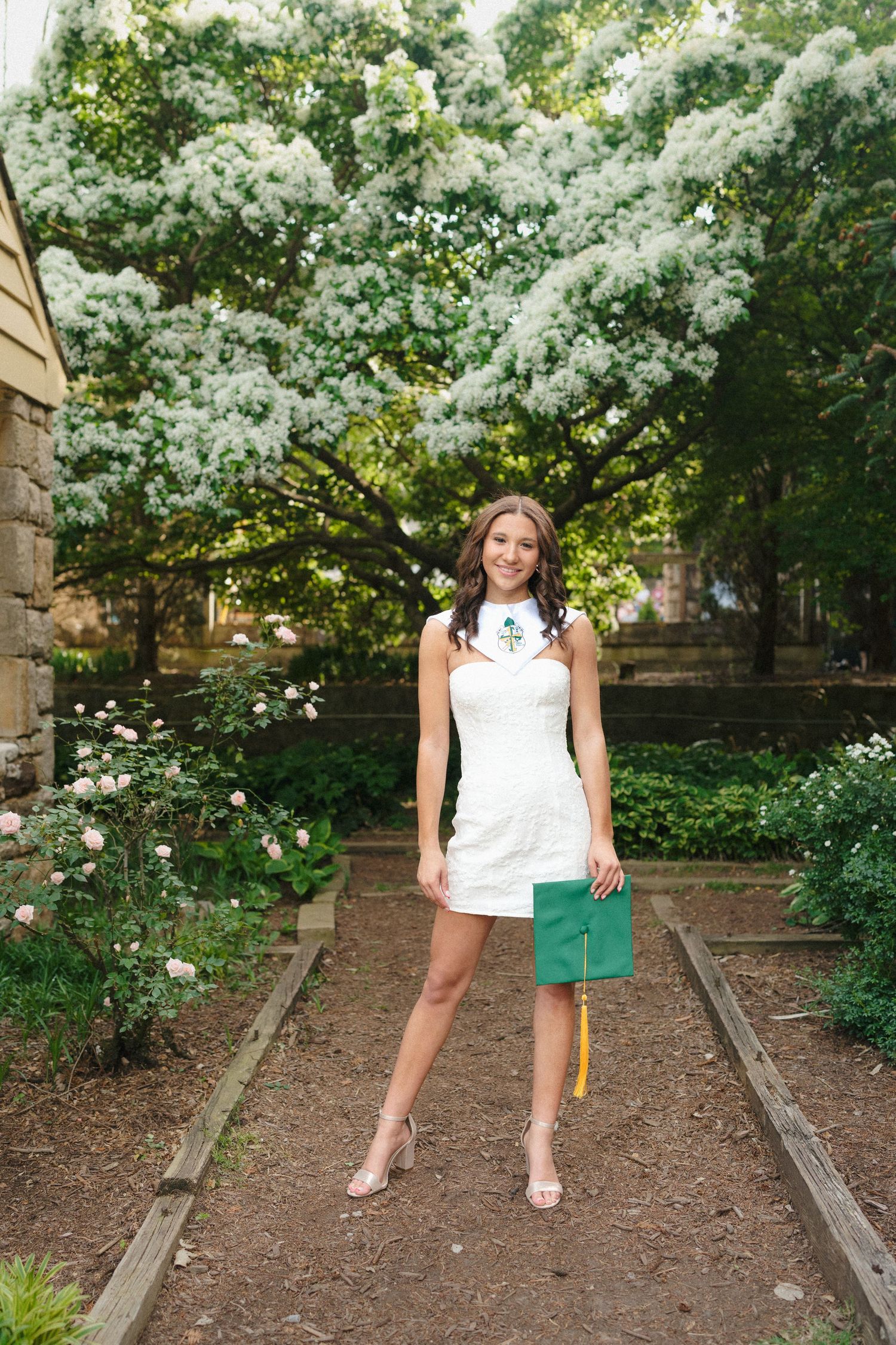 High school senior girl wearing a stole and holding her cap at the Raleigh Rose Garden in Raleigh, North Carolina.