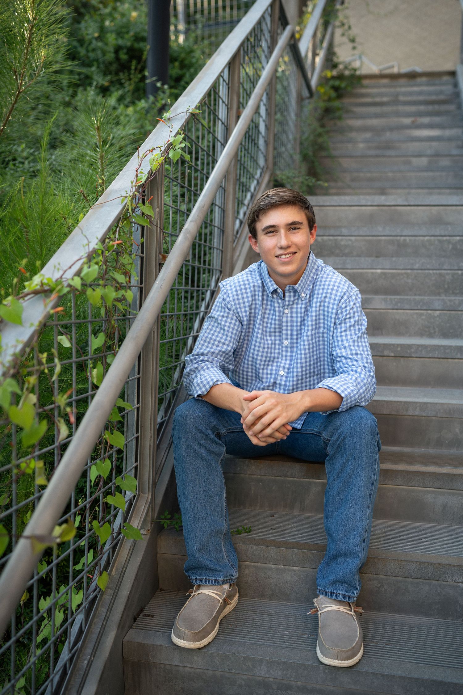 Sitting on outdoor stairs in a blue checkered shirt at NCMA during his senior photo session