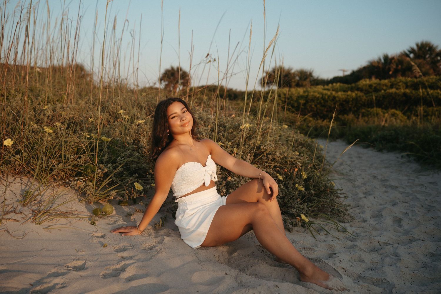 High school senior girl sitting in the sand on Folly Beach, South Carolina during her senior session.
