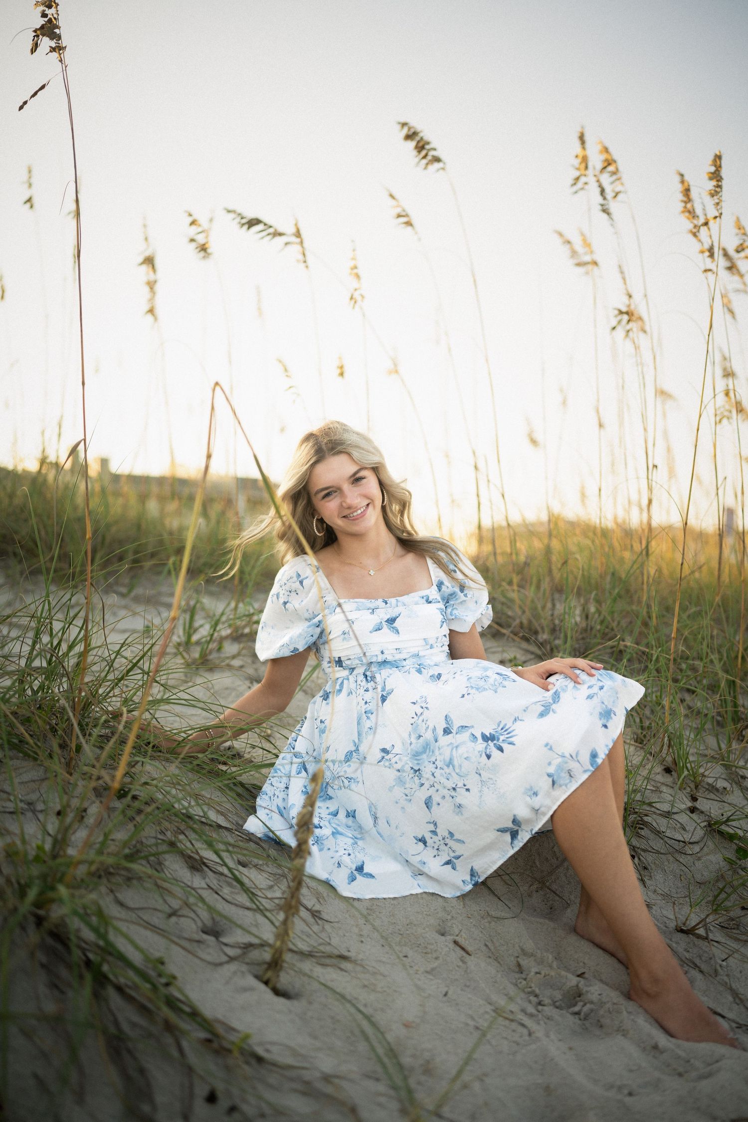 Sydney's senior photo session on Wilmington, NC beach, sitting in the sand during golden hour
