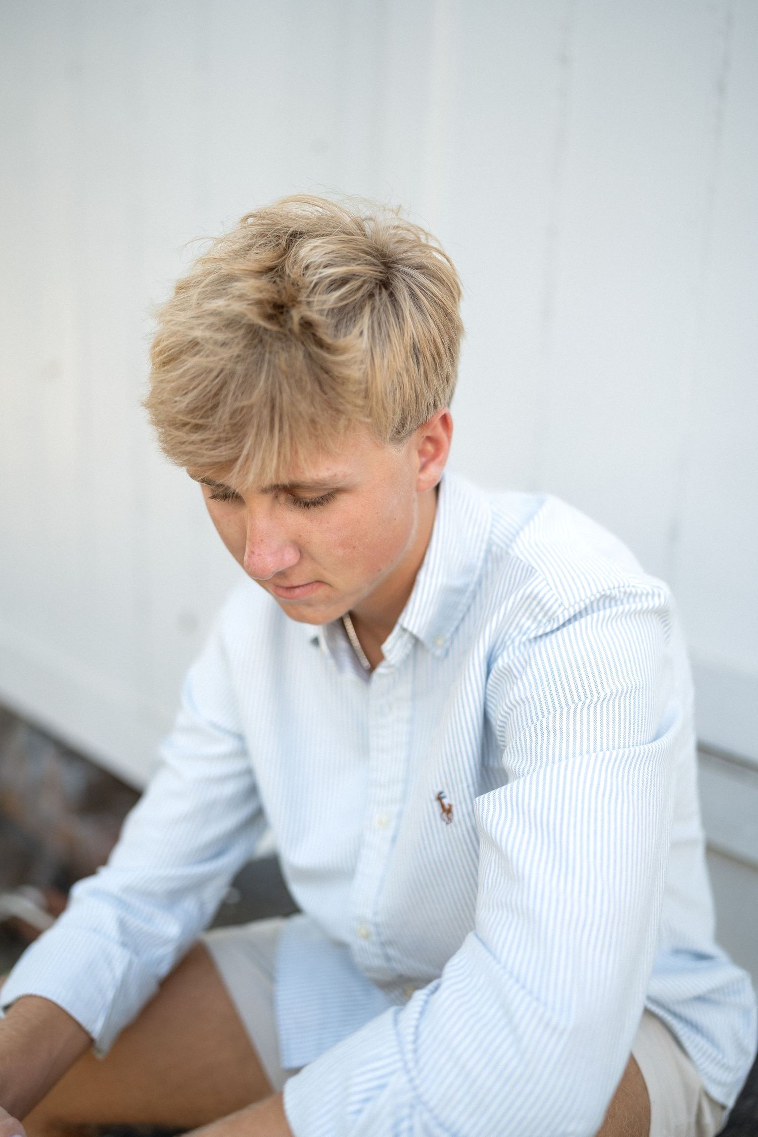 High school senior boy in striped shirt and khaki shorts photographed at family barn property
