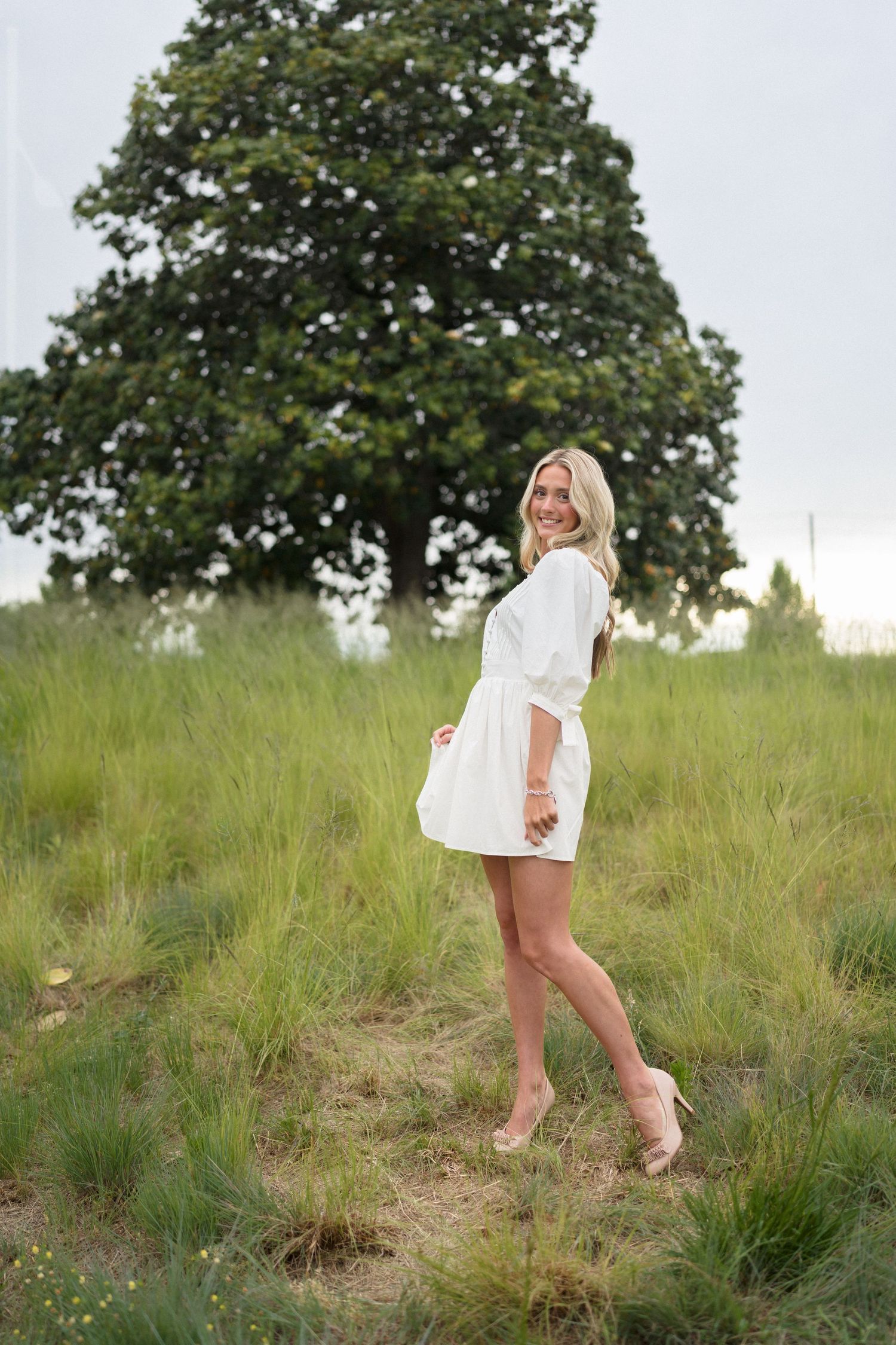 High school senior girl in a white dress standing in the grass at the North Carolina Museum of Art in Raleigh.