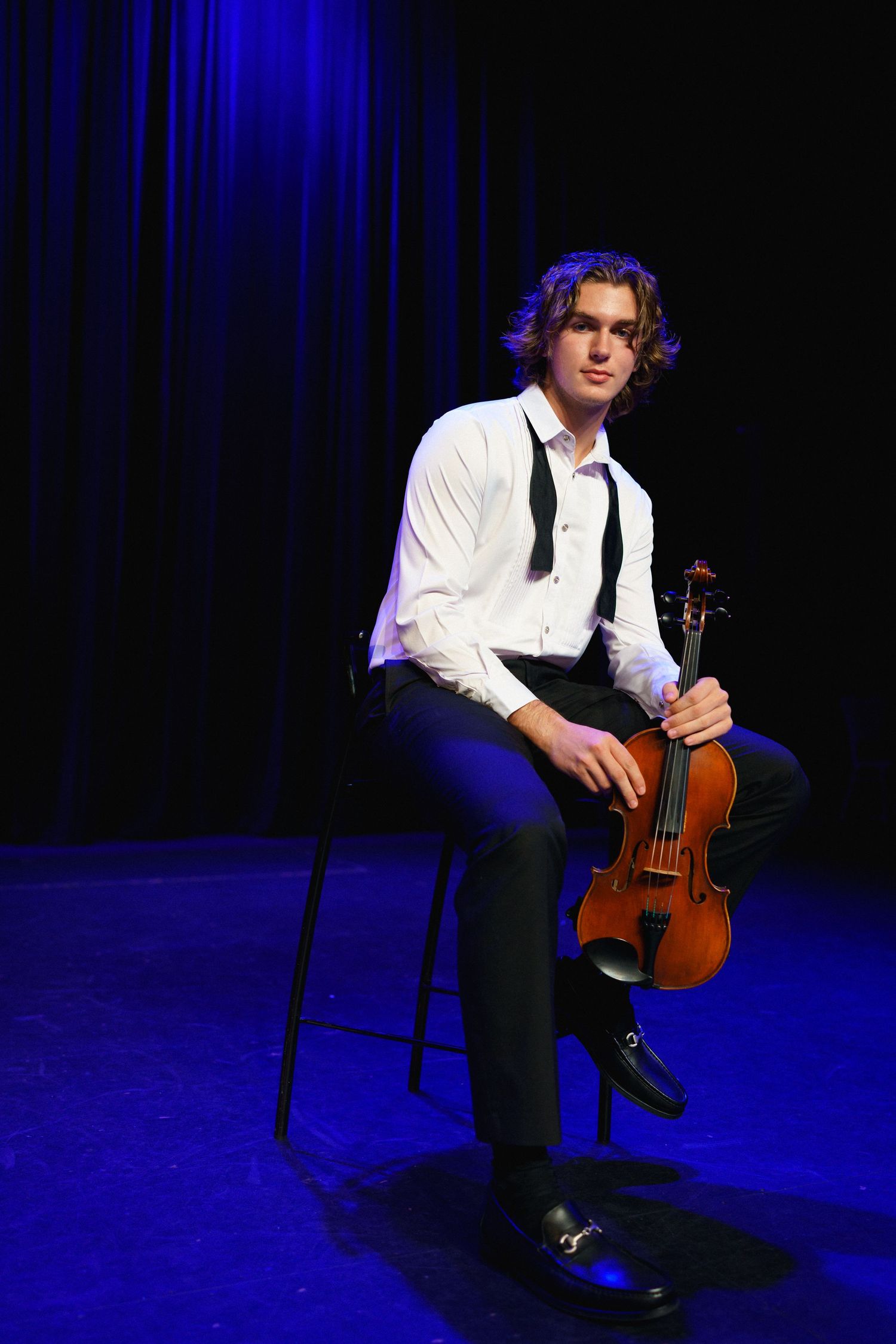Senior boy violin portrait under blue stage lights at The Clayton Center in Clayton, NC