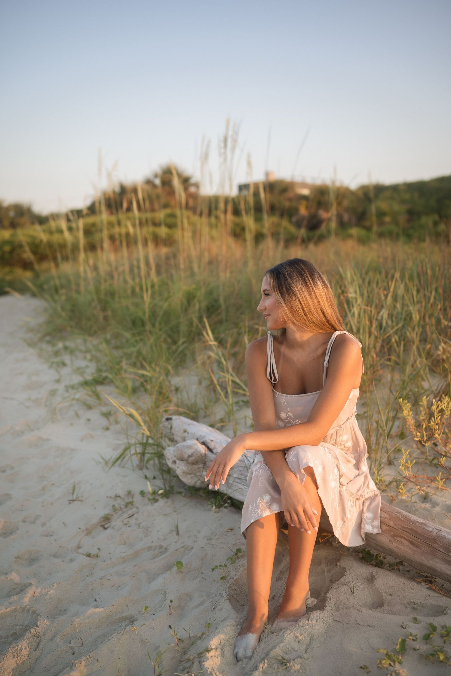 Teen senior photographed by the water in a tan dress with white flowers at Folly Beach.
