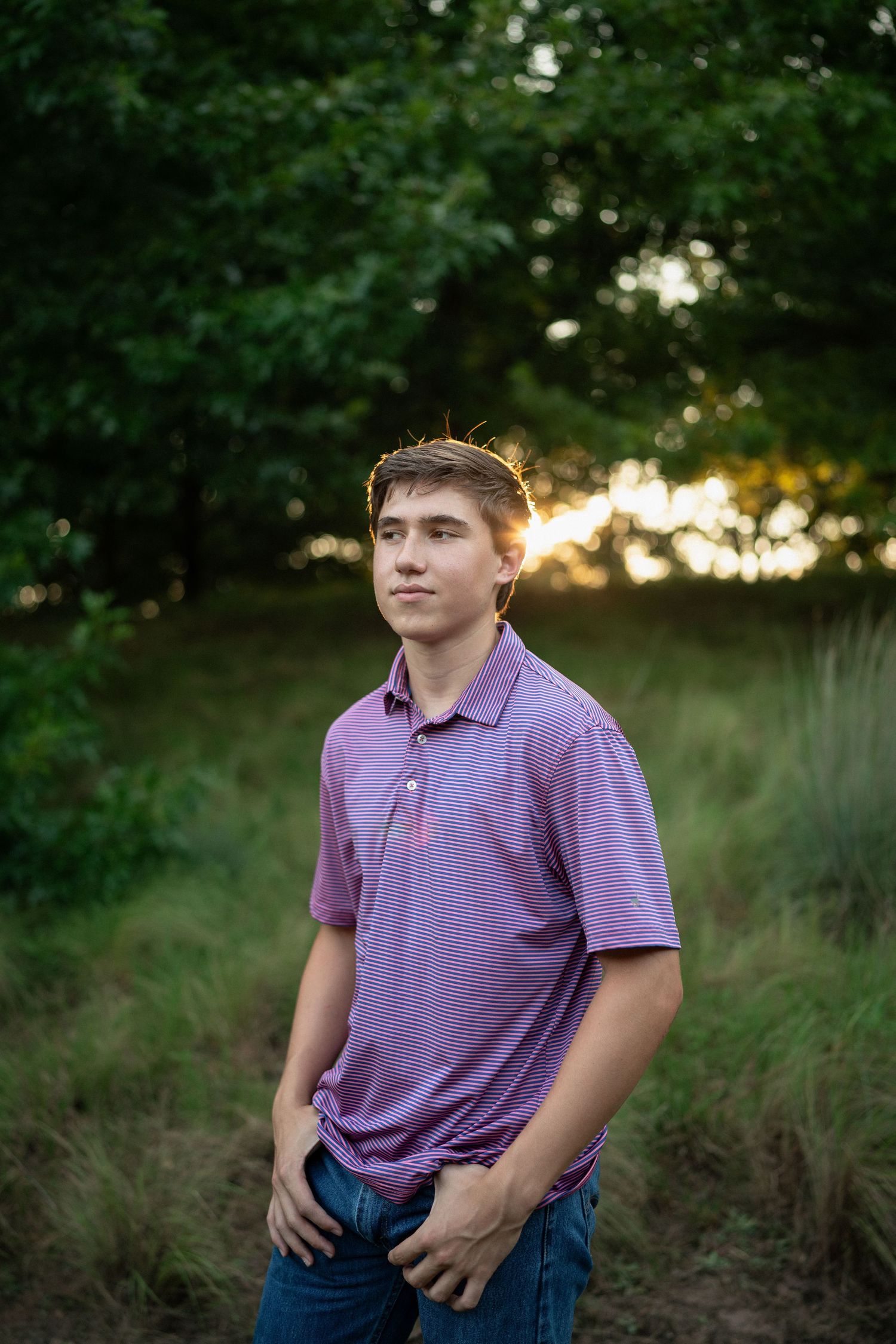 standing in grassy fields at sunset wearing a purple polo shirt during NCMA senior session