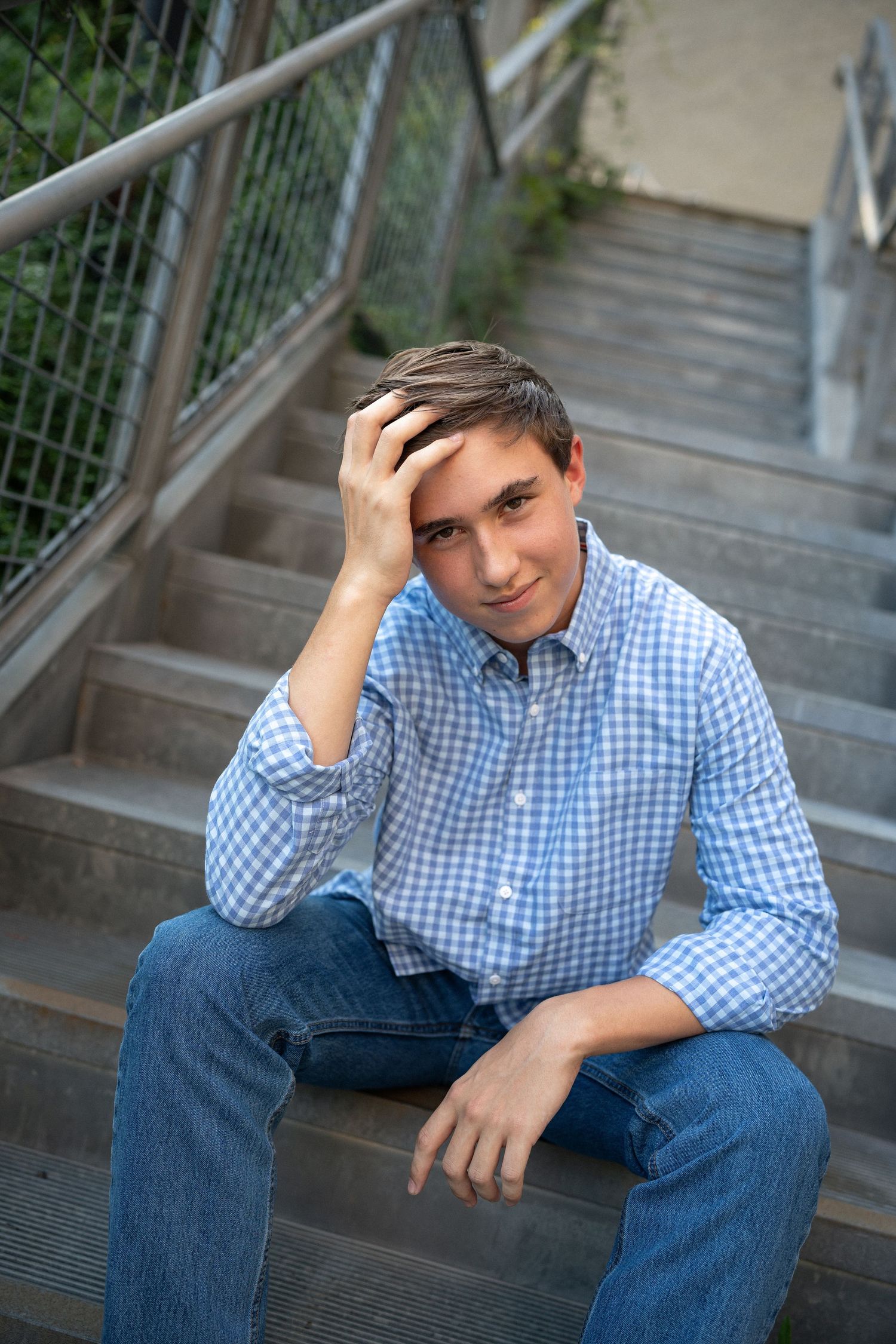 Sitting on outdoor stairs in a blue checkered shirt at NCMA during his senior photo session