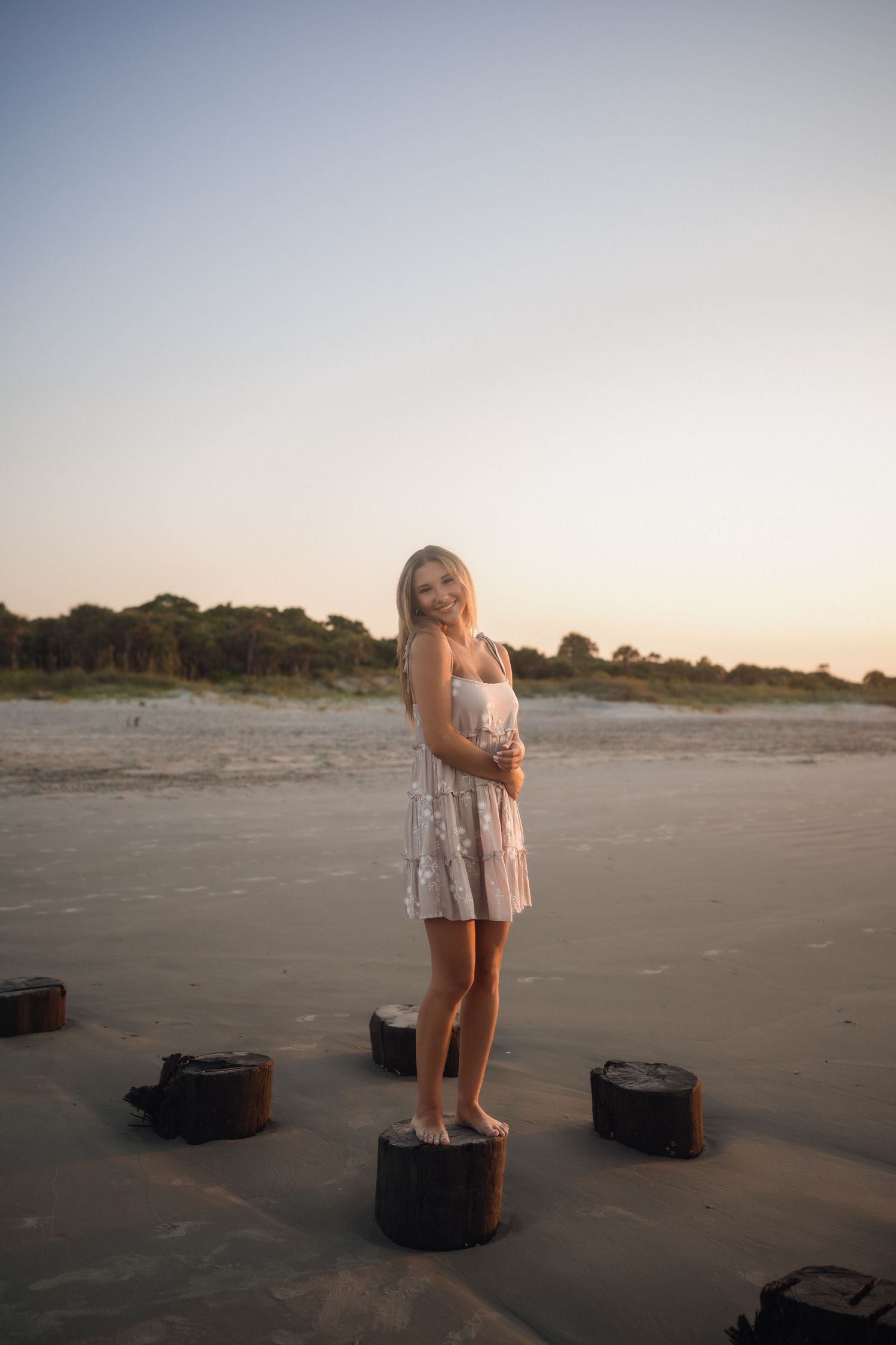 Teen senior photographed by the water in a tan dress with white flowers at Folly Beach.