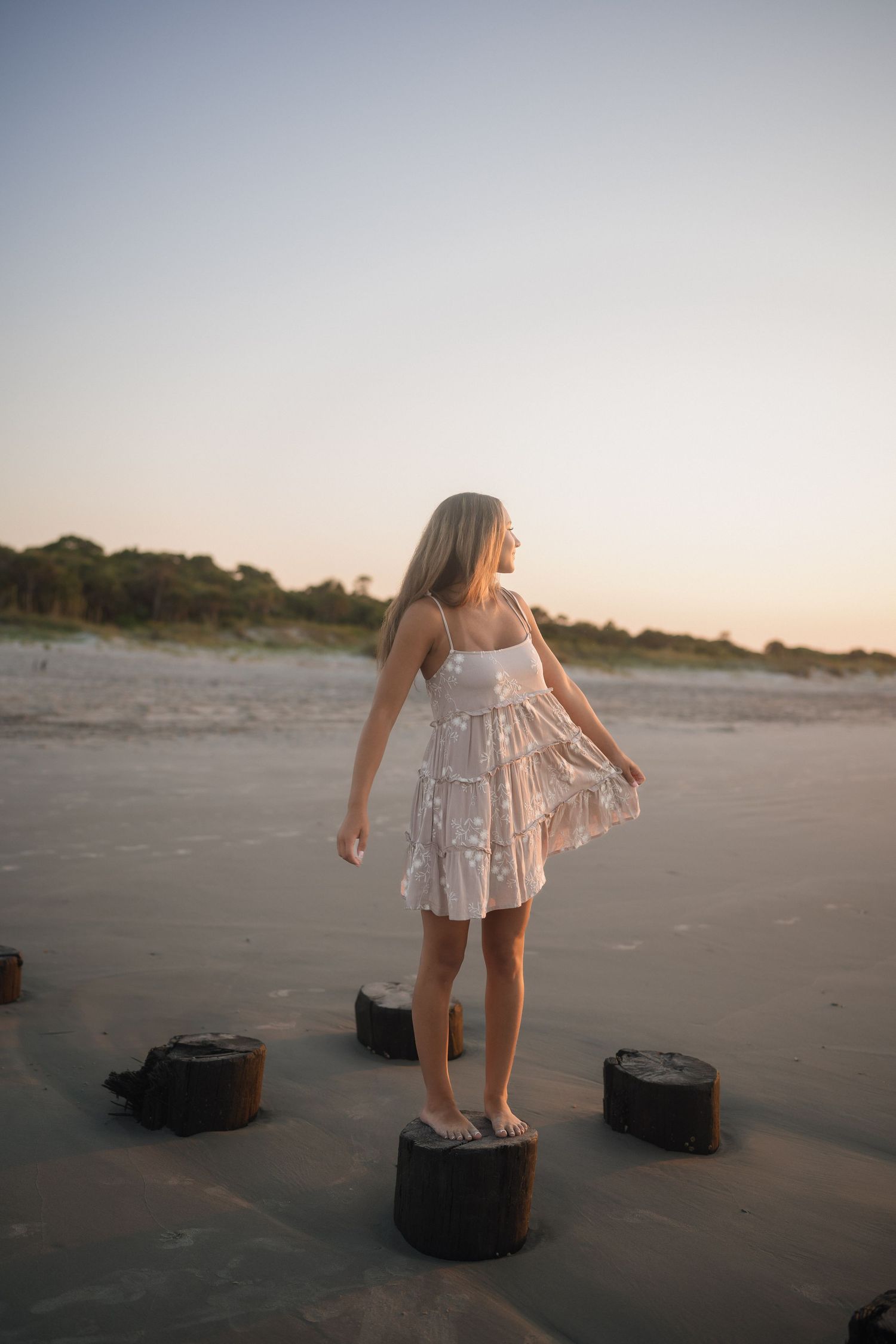 Teen senior photographed by the water in a tan dress with white flowers at Folly Beach.