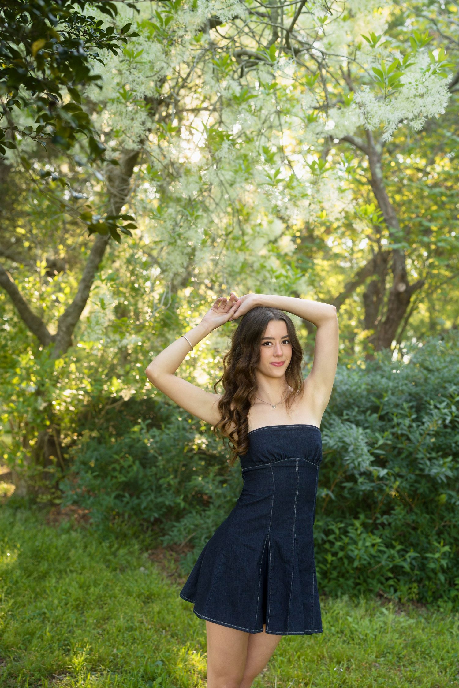 High school senior girl in a denim dress framing her face with her hands at Horseshoe Farm Preserve in Wake Forest.