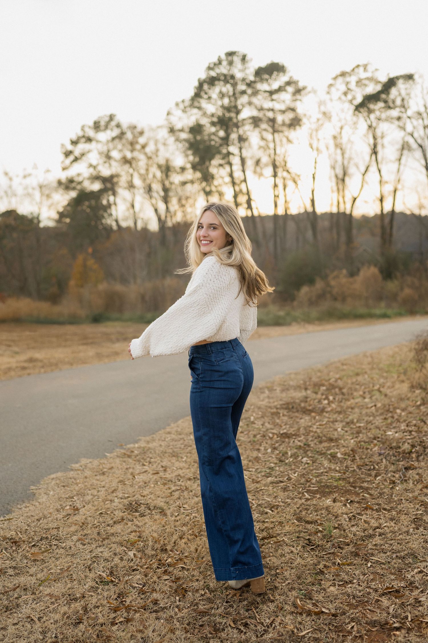 High school senior girl walking away and looking back at Sugg Farm in Holly Springs, North Carolina during a winter session.