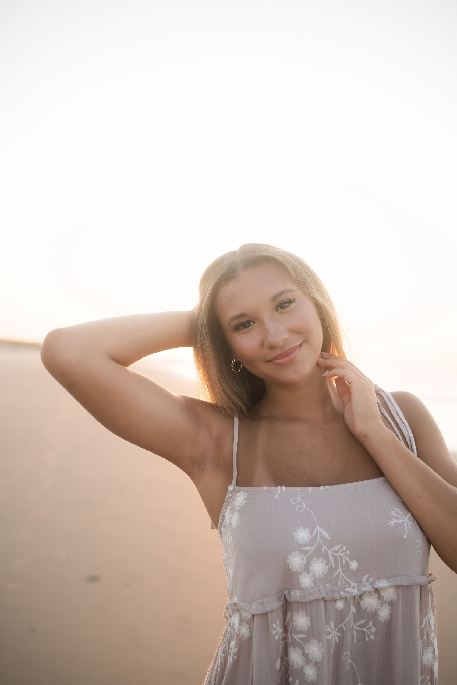 Teen senior photographed by the water in a tan dress with white flowers at Folly Beach.