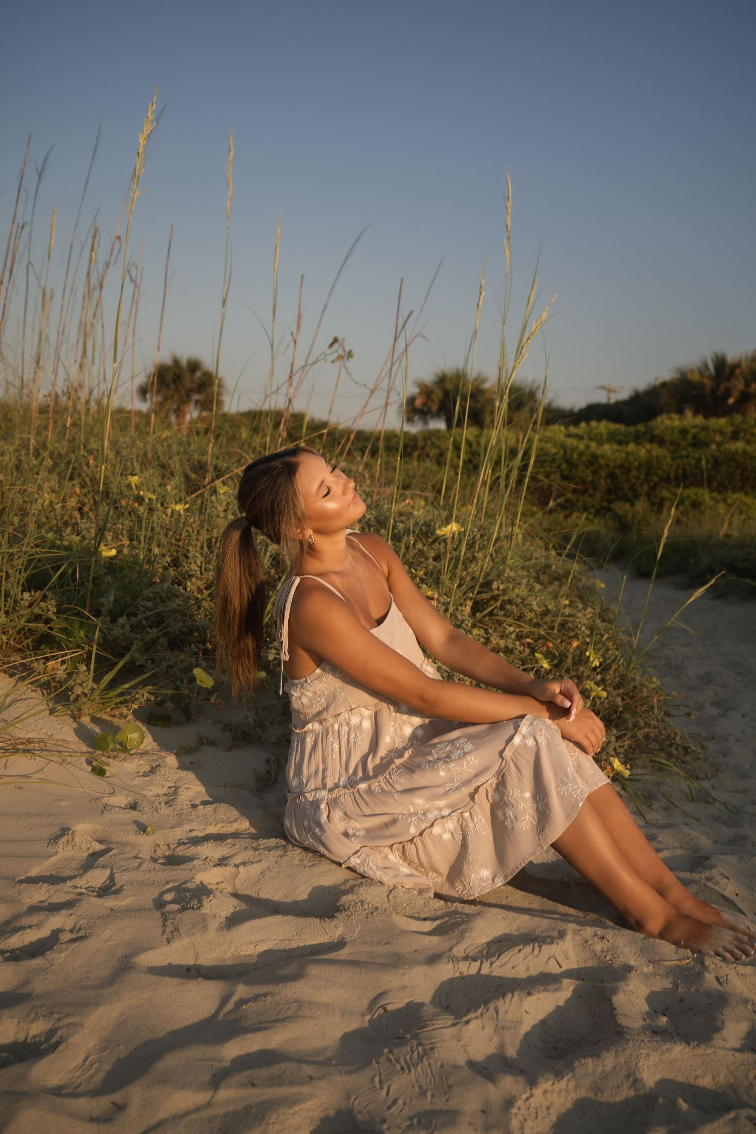 Teen senior photographed by the water in a tan dress with white flowers at Folly Beach.