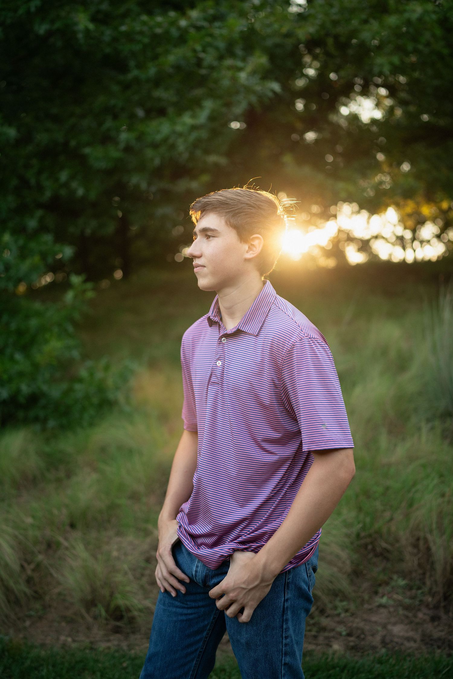 standing in grassy fields at sunset wearing a purple polo shirt during NCMA senior session