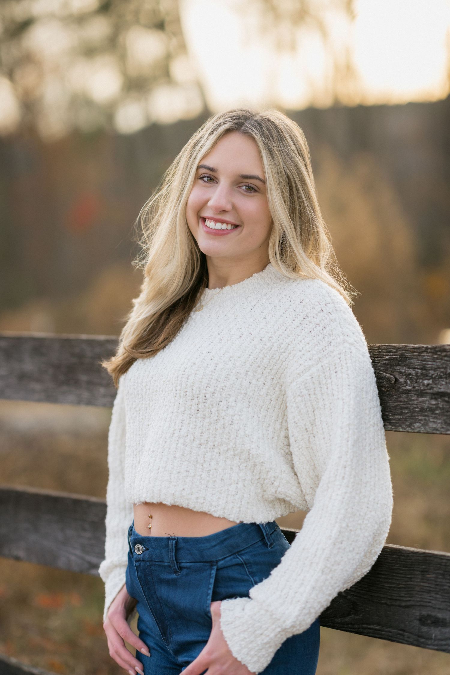 High school senior girl in a white sweater leaning on a fence at Sugg Farm in Holly Springs, North Carolina.