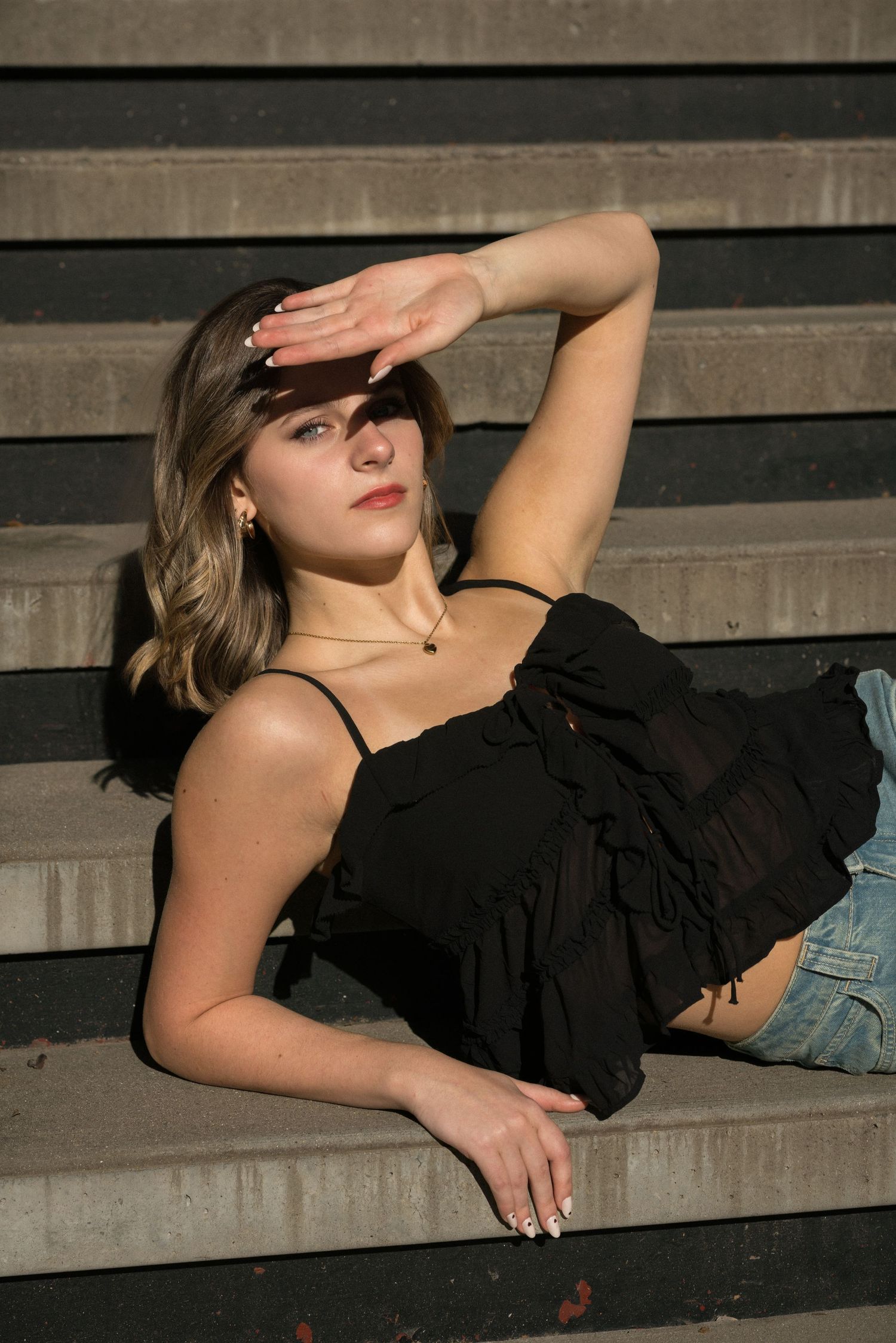 High school senior girl laying on stairs and shielding her eyes from the sun at American Tobacco Campus in Durham.