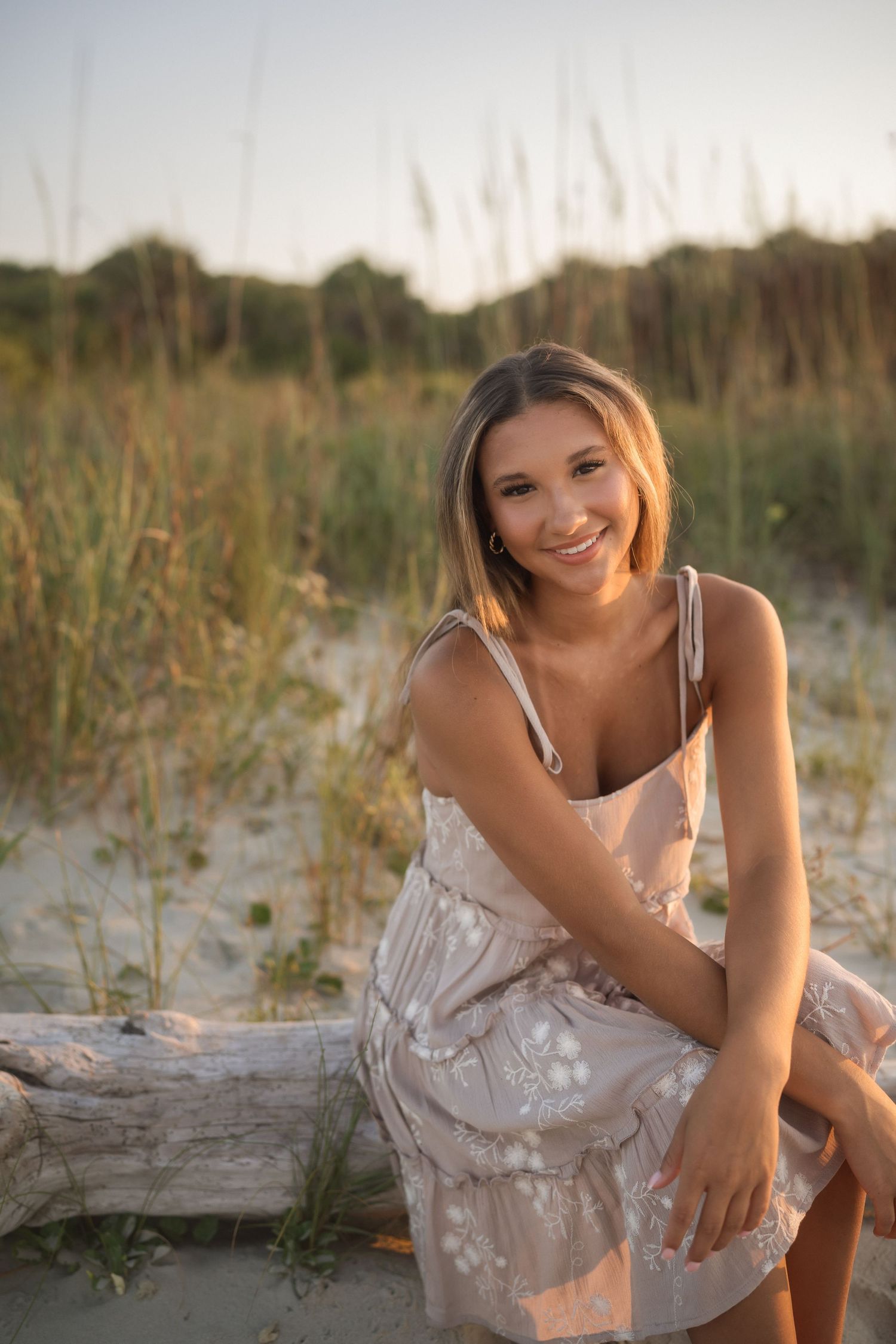 Teen senior photographed by the water in a tan dress with white flowers at Folly Beach.