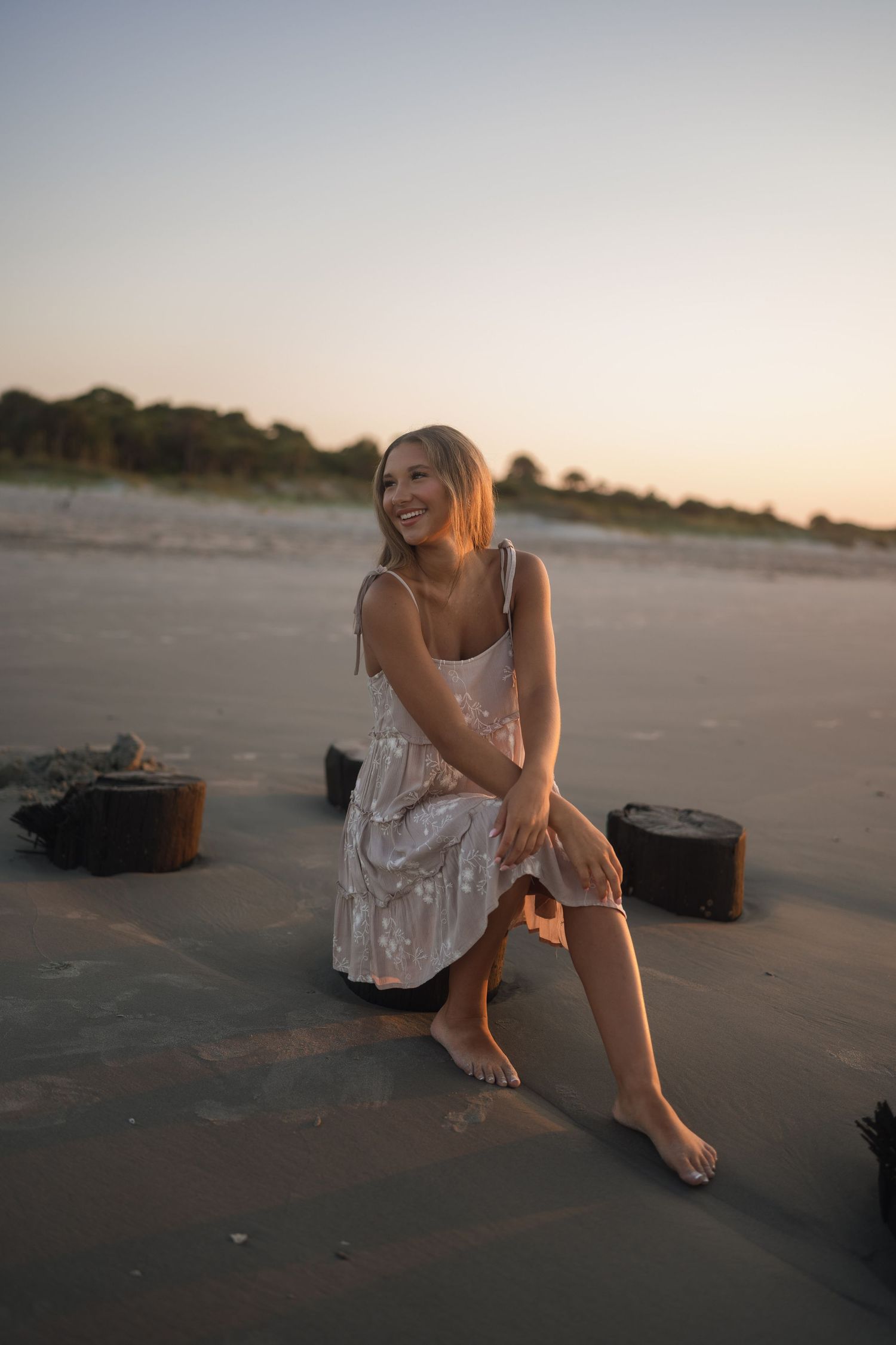 Teen senior photographed by the water in a tan dress with white flowers at Folly Beach.