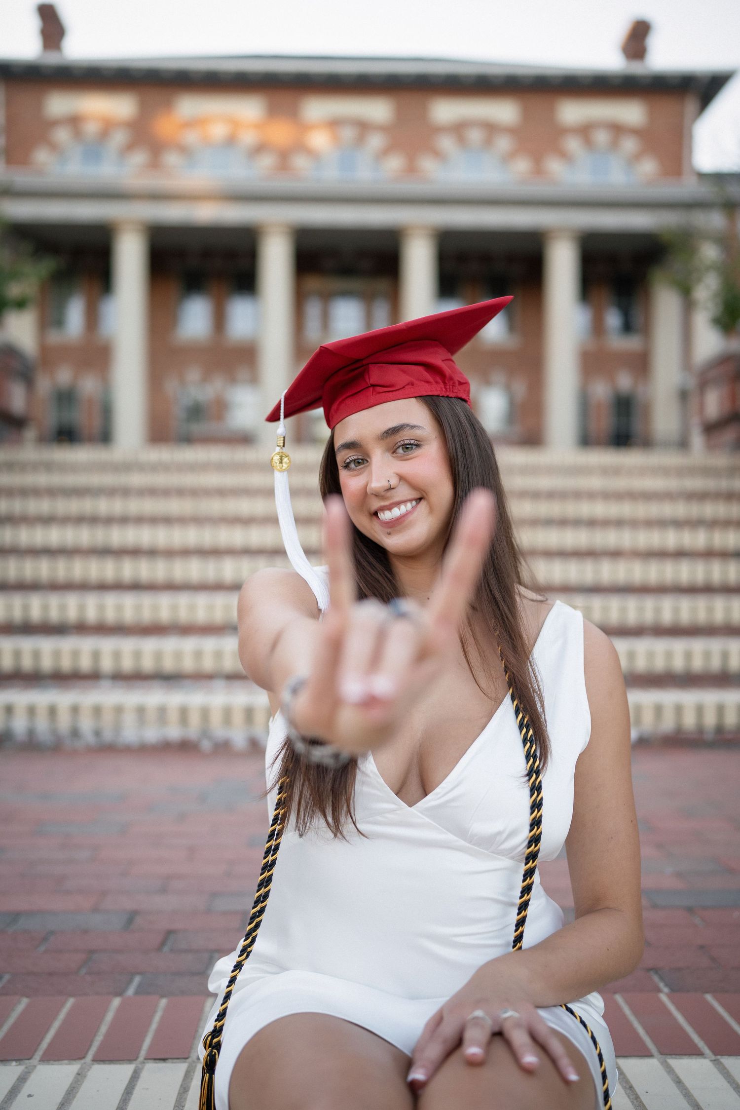 NC State graduate in red cap and gown giving Wolfpack sign at Court of Carolina in Raleigh, NC