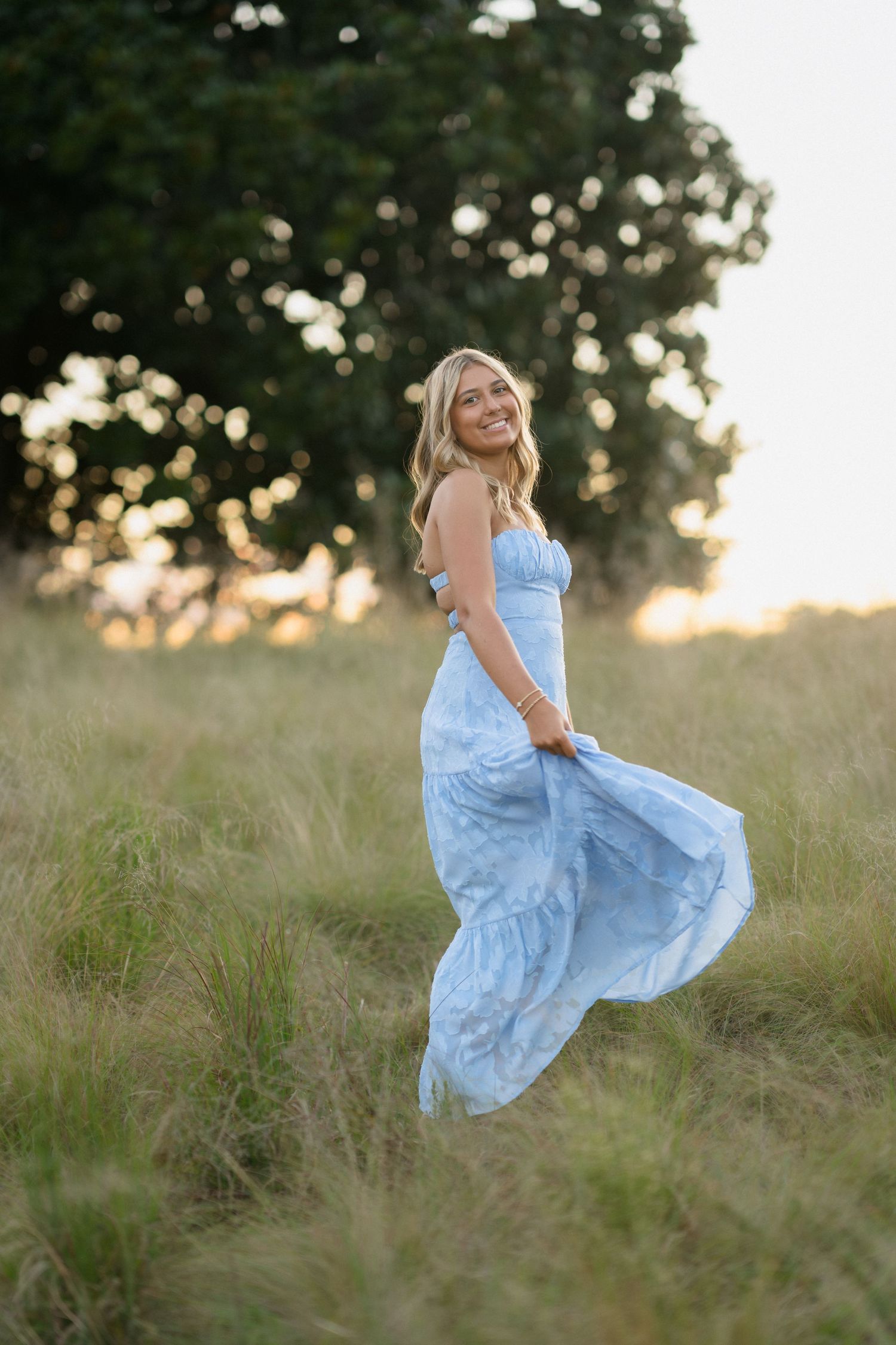 High school senior girl playing with her dress in the grass during her senior session at the North Carolina Museum of Art in Raleigh.