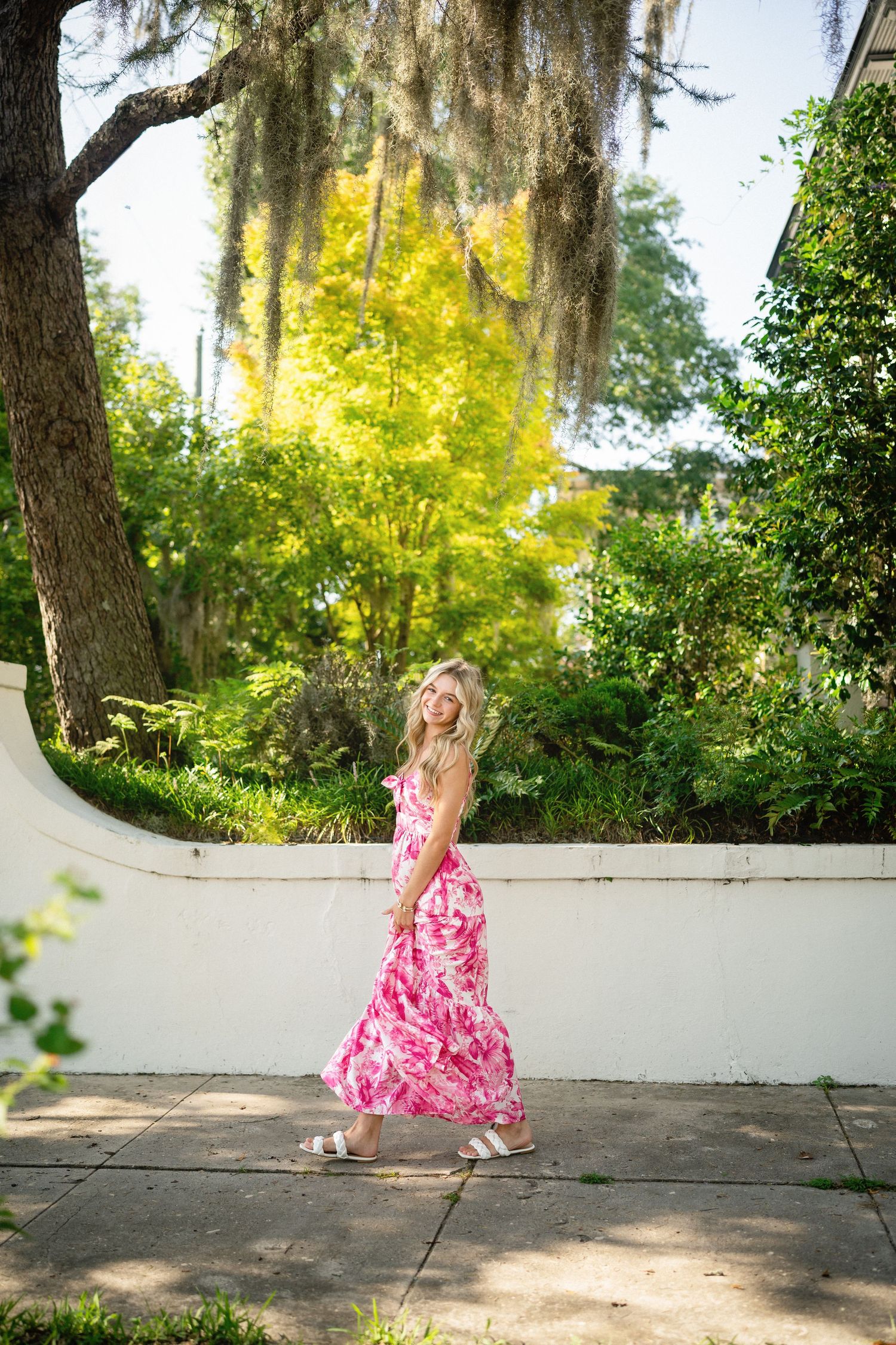Senior photo of Sydney walking in front of a stunning residence in Wilmington, NC, draped with Spanish moss.
