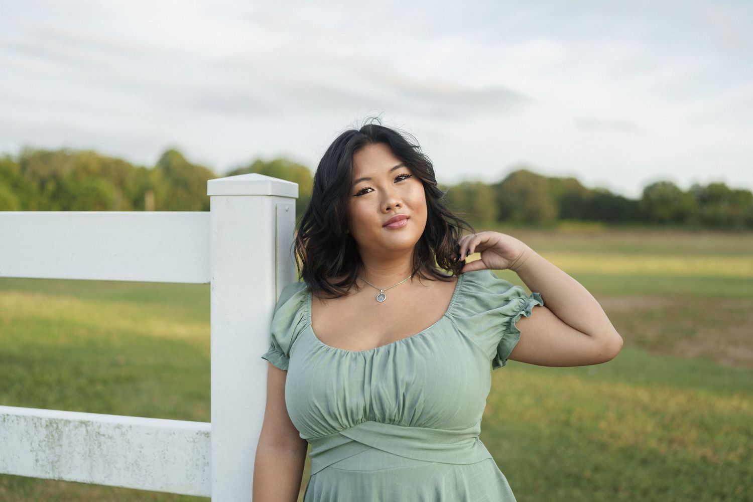 High school senior girl in a green dress standing by a white fence at Dix Park in Raleigh, North Carolina.