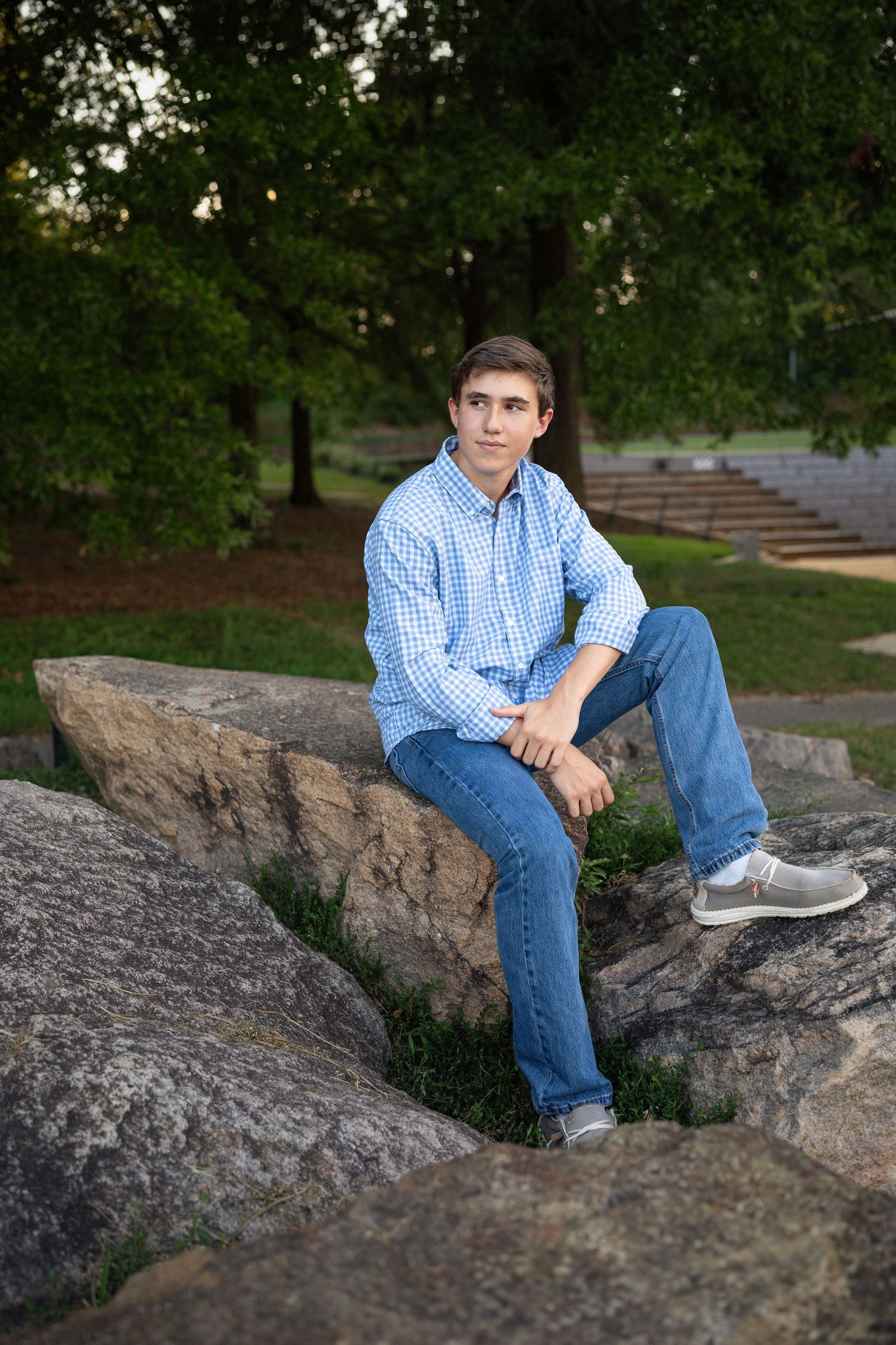 Sitting on large rocks in a blue checkered shirt and jeans during NCMA senior session