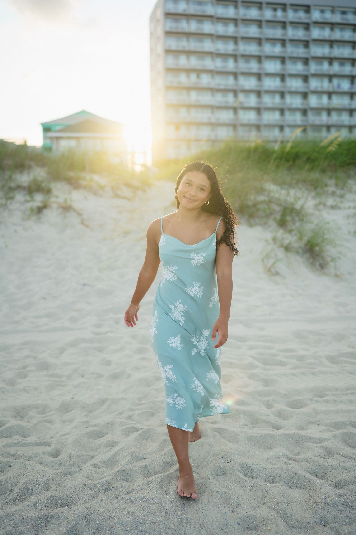 High school senior girl walking along the beach at sunset with the sun behind her at Carolina Beach, North Carolina.
