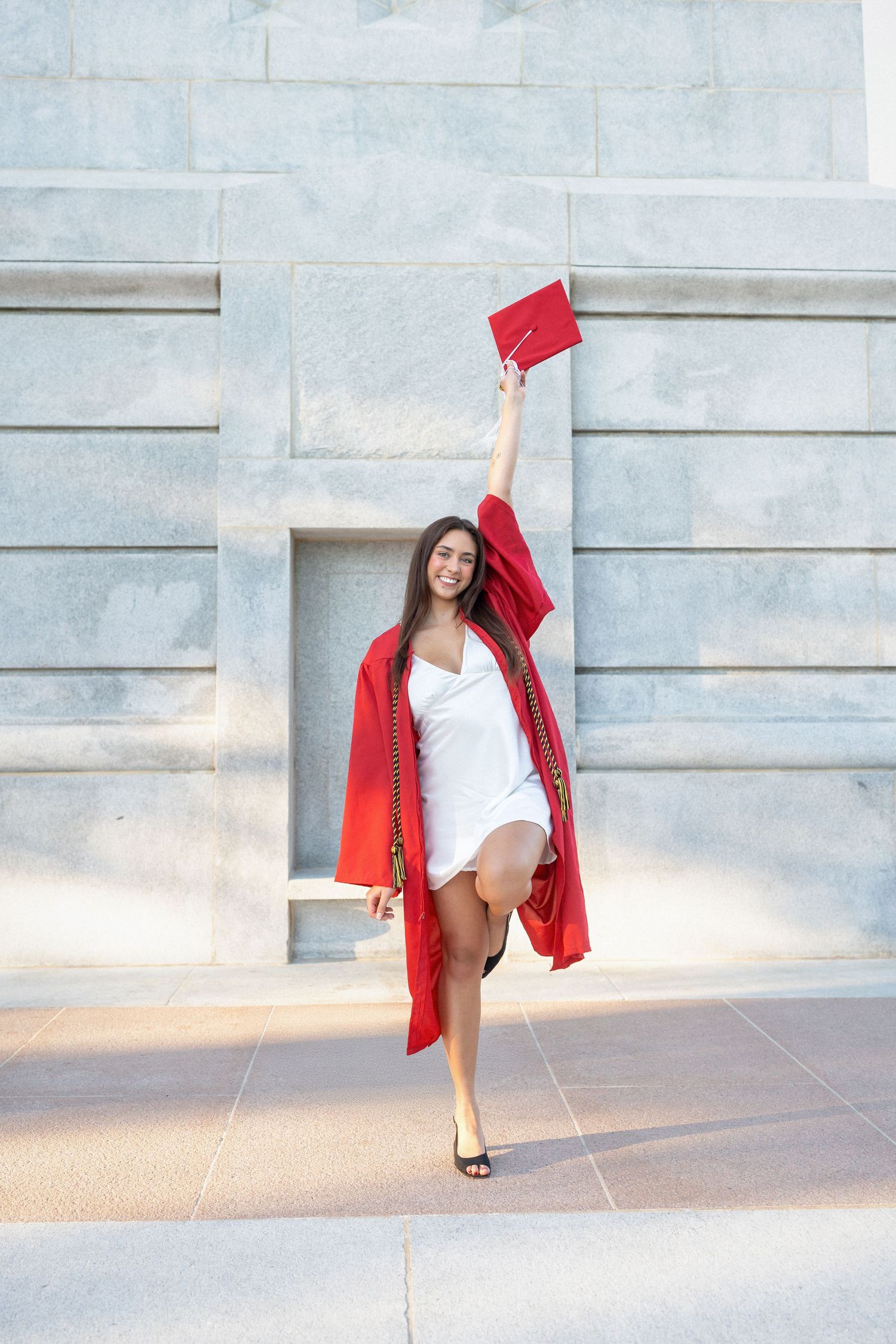 NC State graduate in red cap and gown giving at bell tower in Raleigh, NC