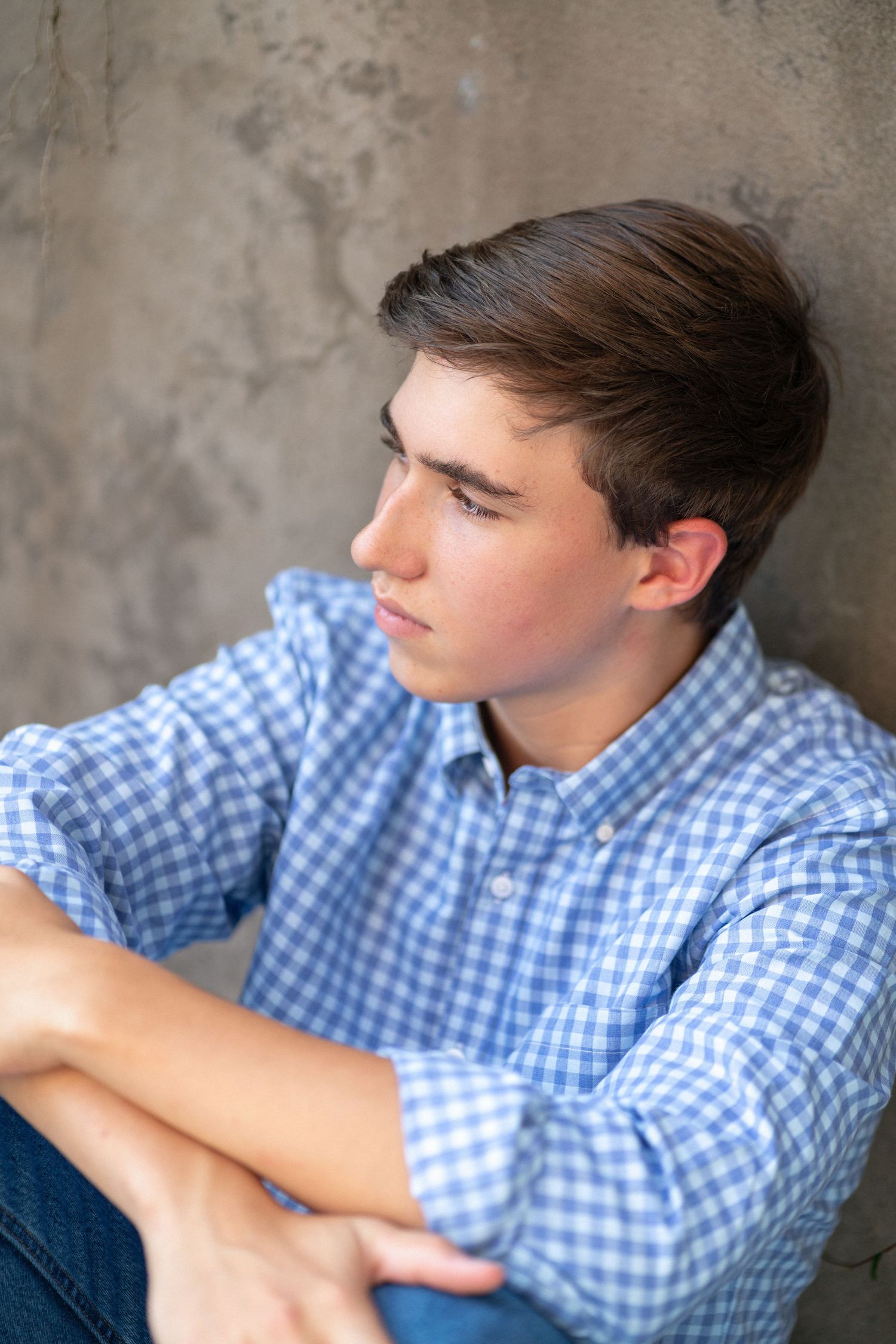 Leaning against a concrete wall in a blue checkered shirt at NCMA for senior photos