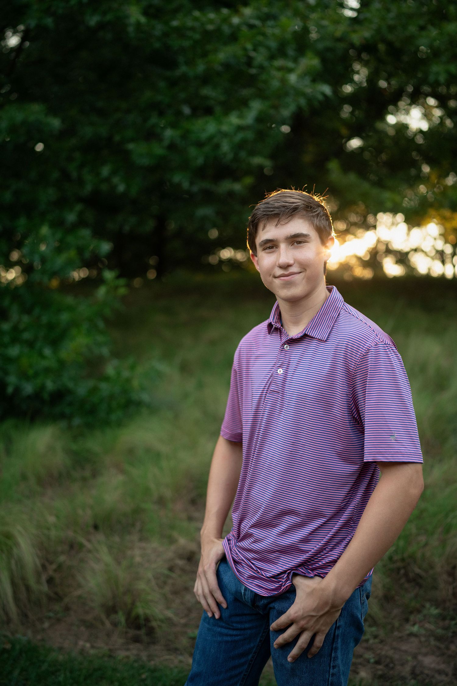 standing in grassy fields at sunset wearing a purple polo shirt during NCMA senior session