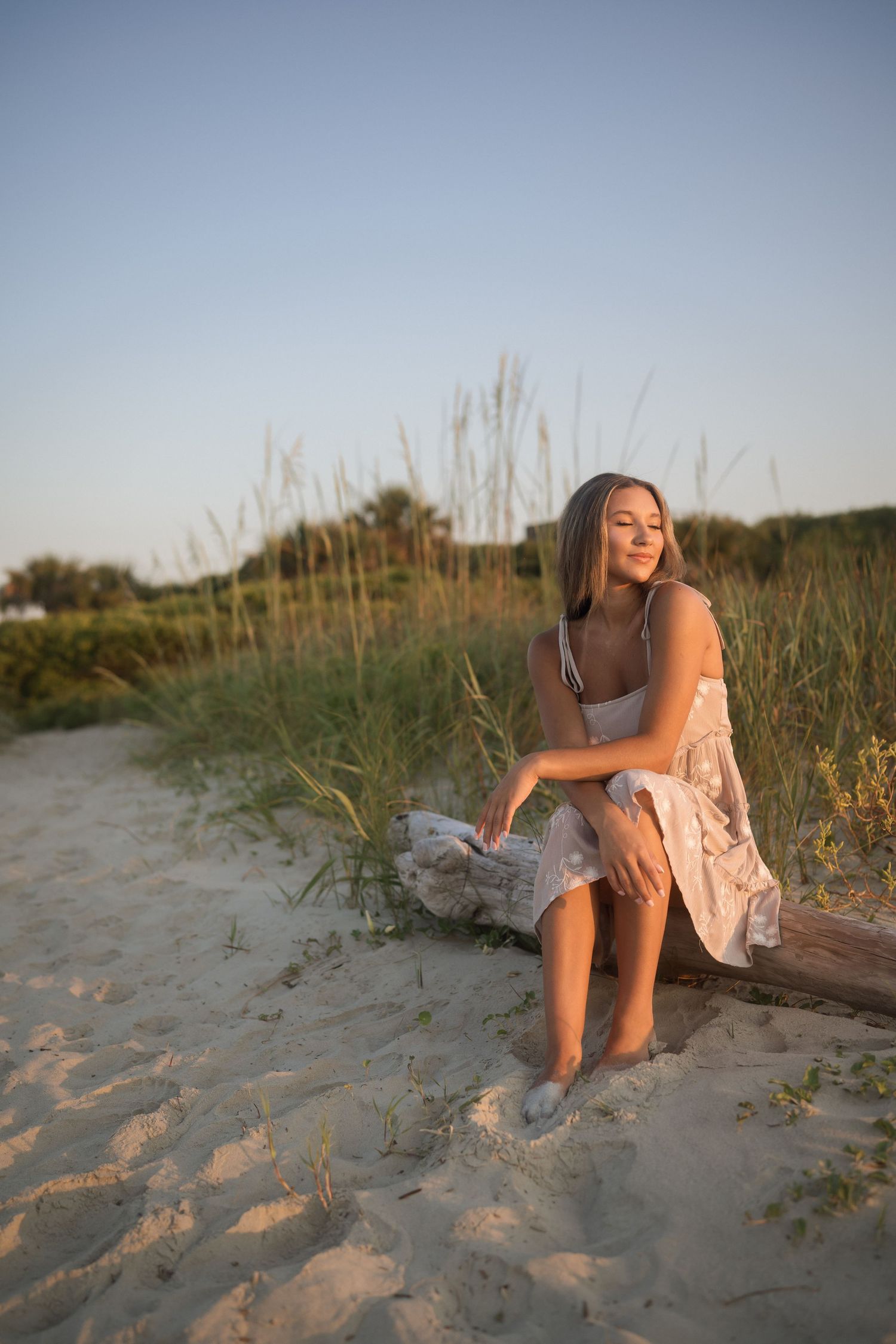 Teen senior photographed by the water in a tan dress with white flowers at Folly Beach.