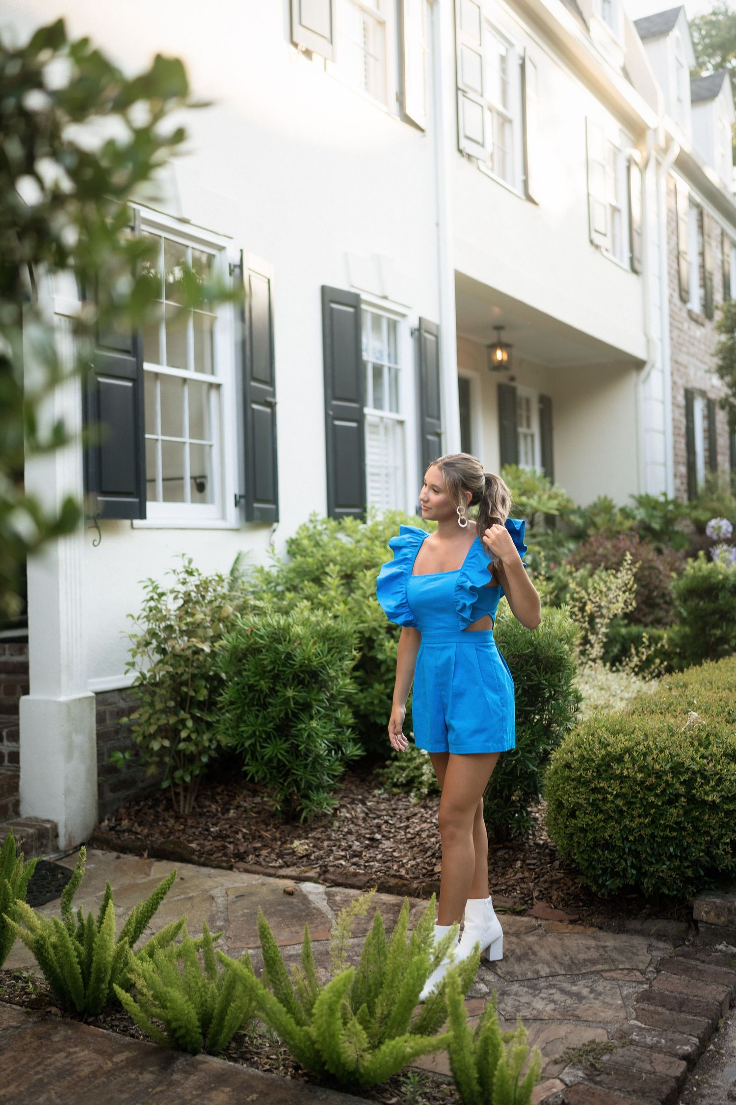 Kaylei posing in a blue jumpsuit on Charleston cobblestone streets – Raleigh NC senior photographer.