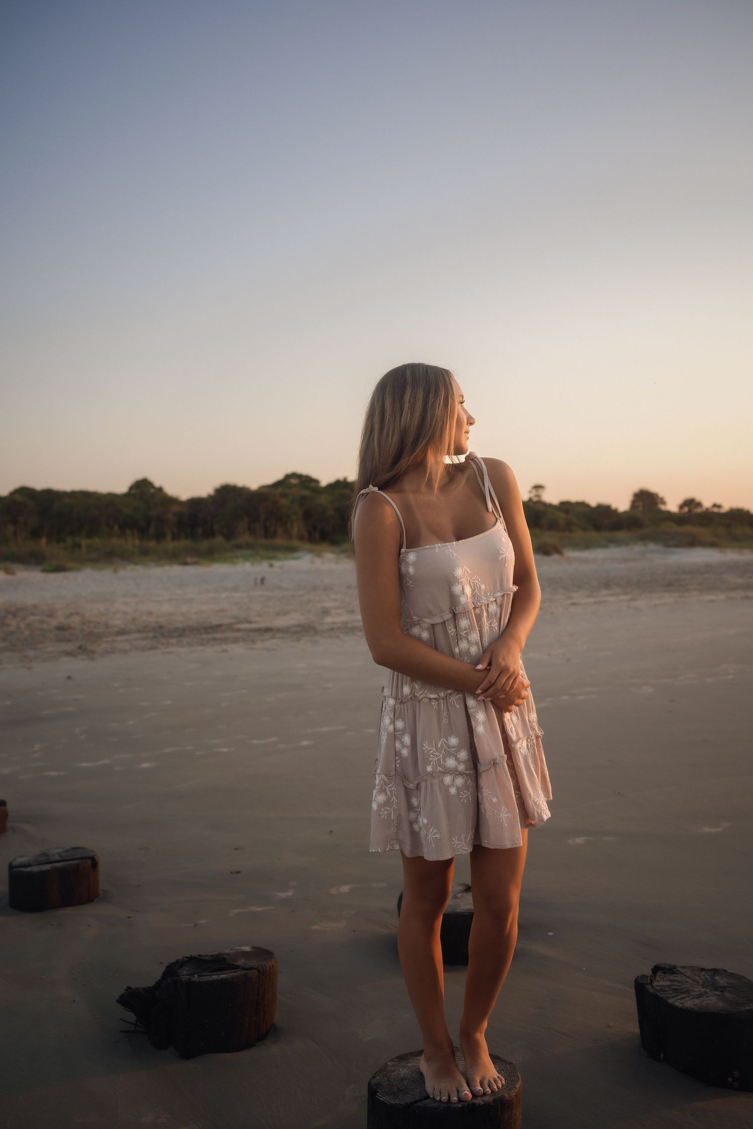 Teen senior photographed by the water in a tan dress with white flowers at Folly Beach.