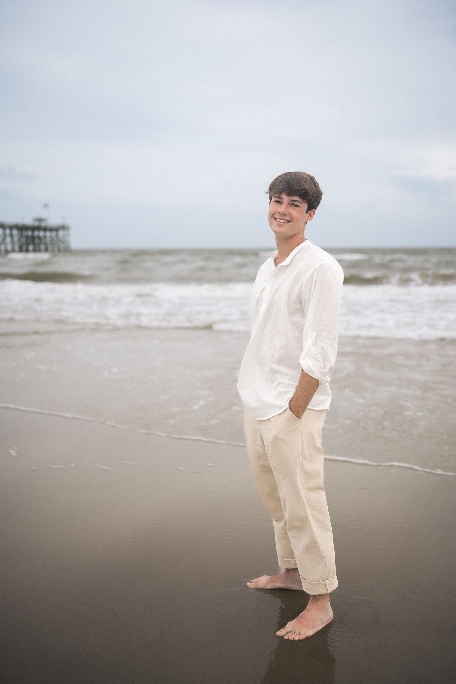 High school senior guy standing on Oak Island Beach with ocean backdrop