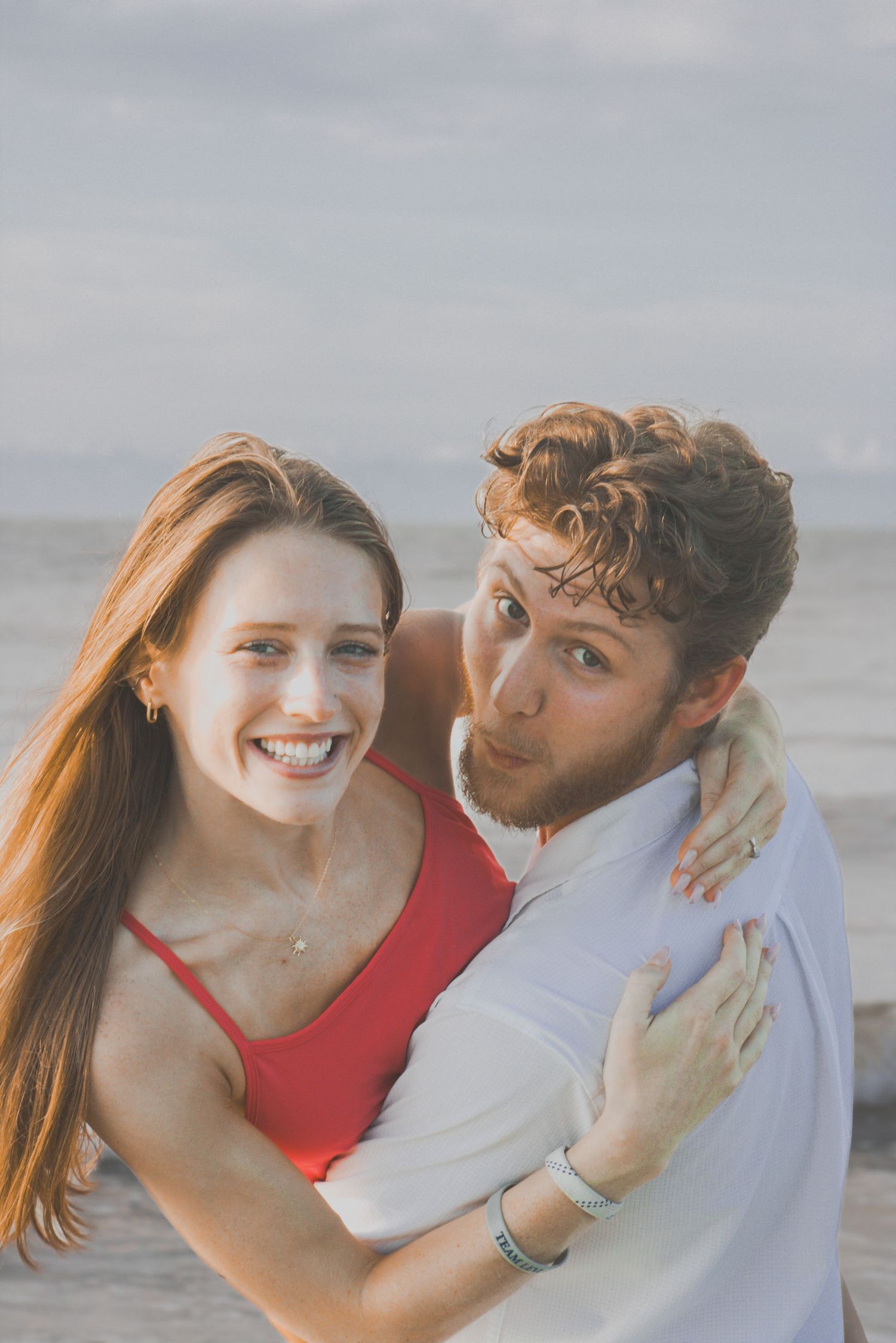 Playful beach photoshoot with warm sunset lighting and ocean waves in the background.