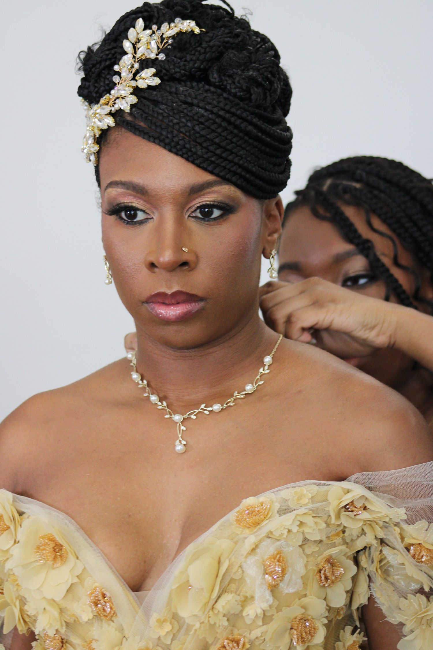 Close-up of bride wearing ornate headpiece, pearl necklace and yellow off-shoulder gown.