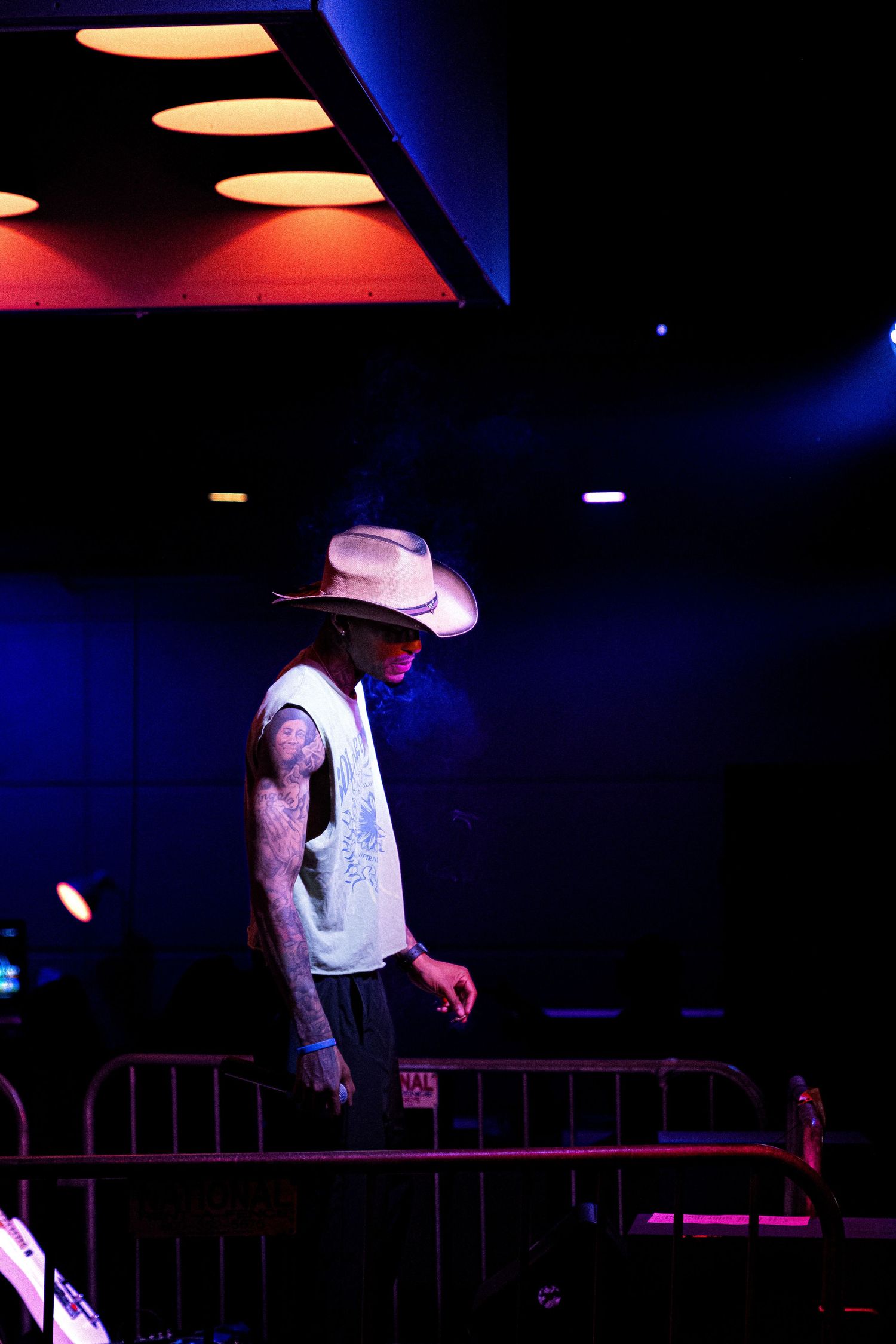 Performer in white cowboy hat illuminated by dramatic red and blue stage lighting.