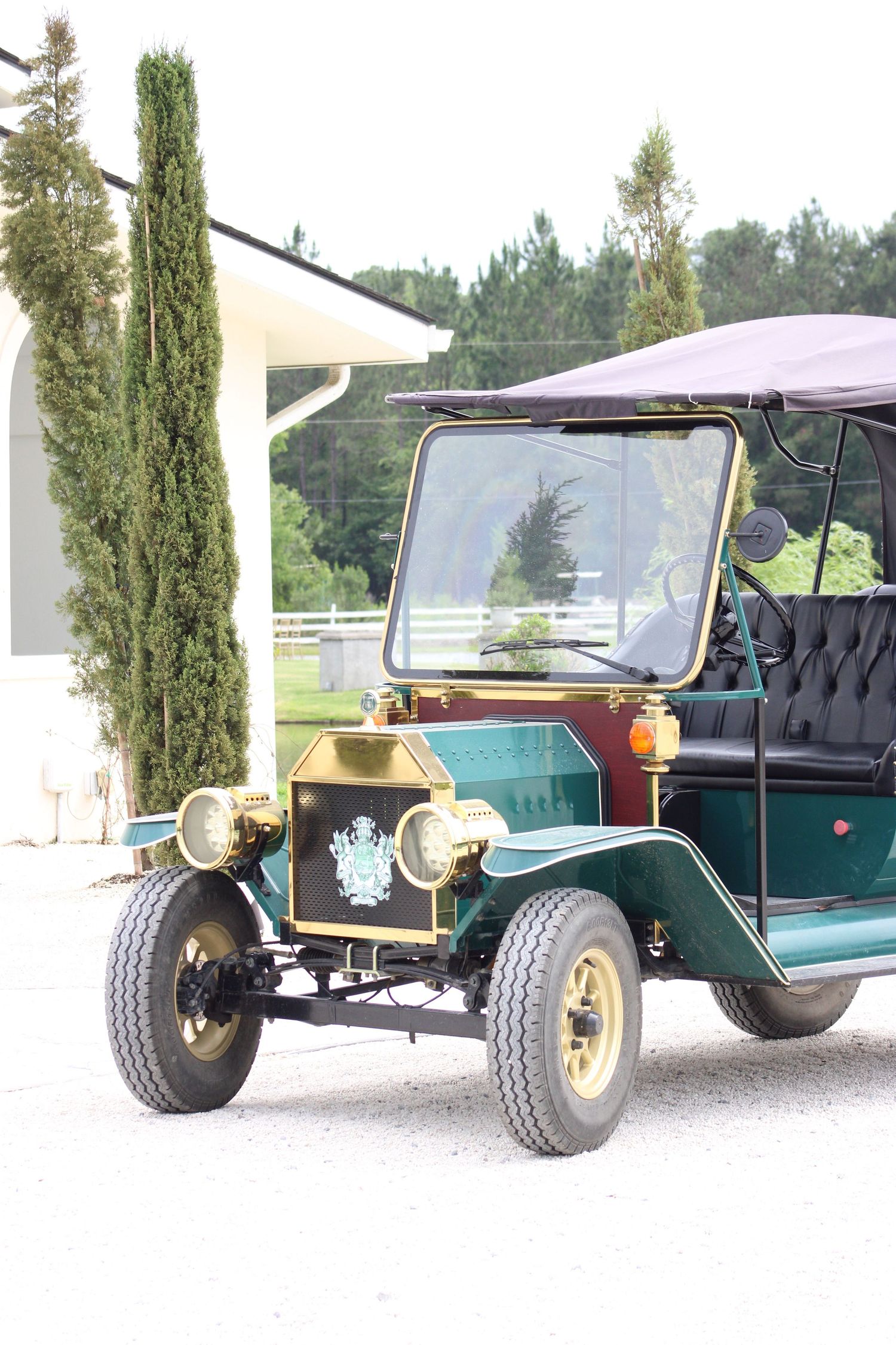 Vintage green antique car parked outside a white building with cypress trees.