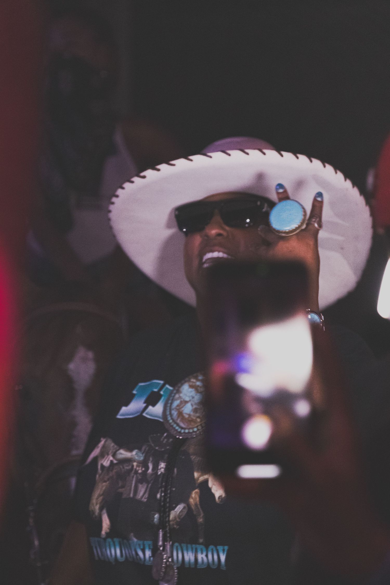 Crowd scene at nightclub with cowboy hats visible under atmospheric lighting.