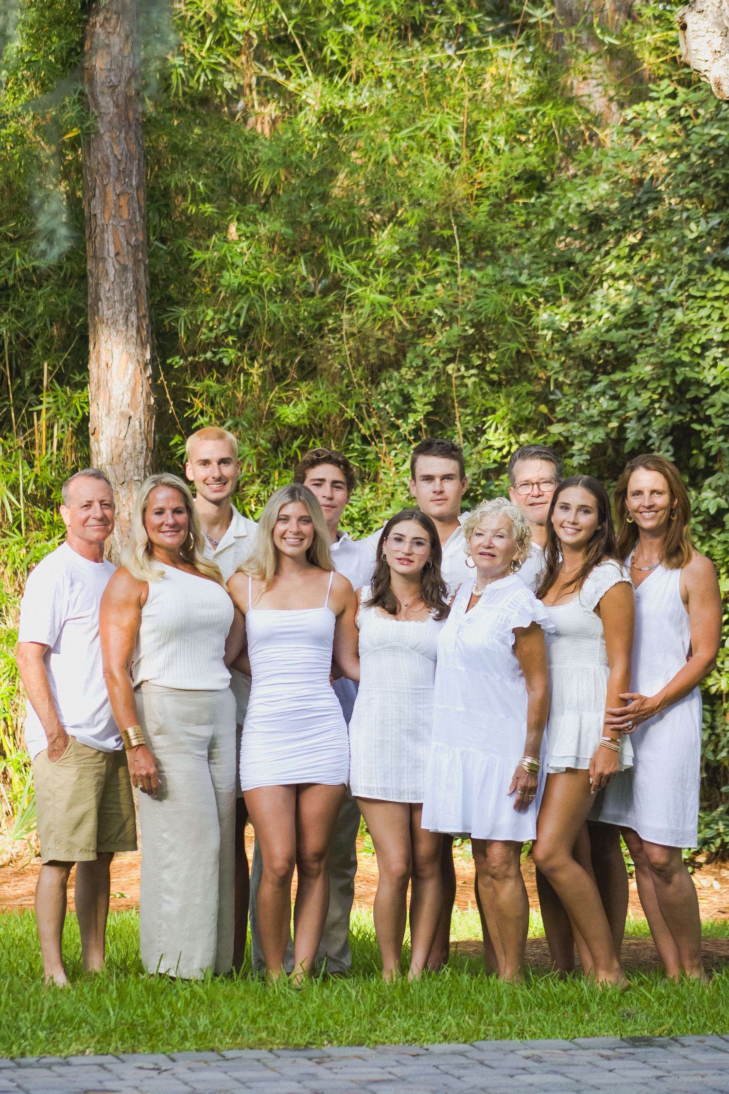 A group in white summer outfits poses together outdoors against a lush green forest backdrop.
