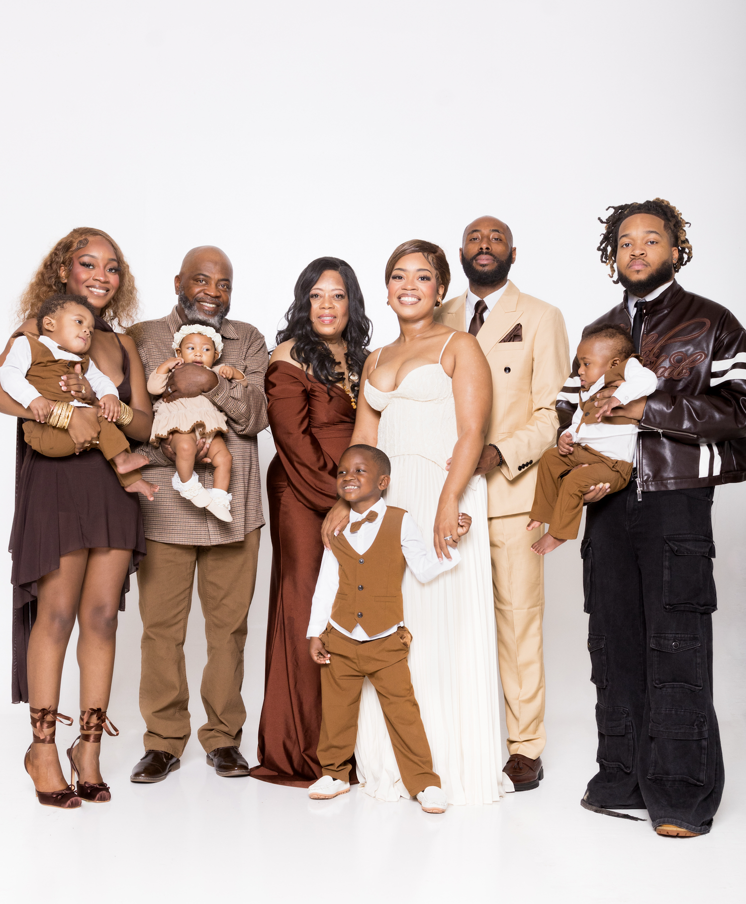 A joyful family portrait with eight people dressed in brown and beige tones, including babies, posing against a white background.