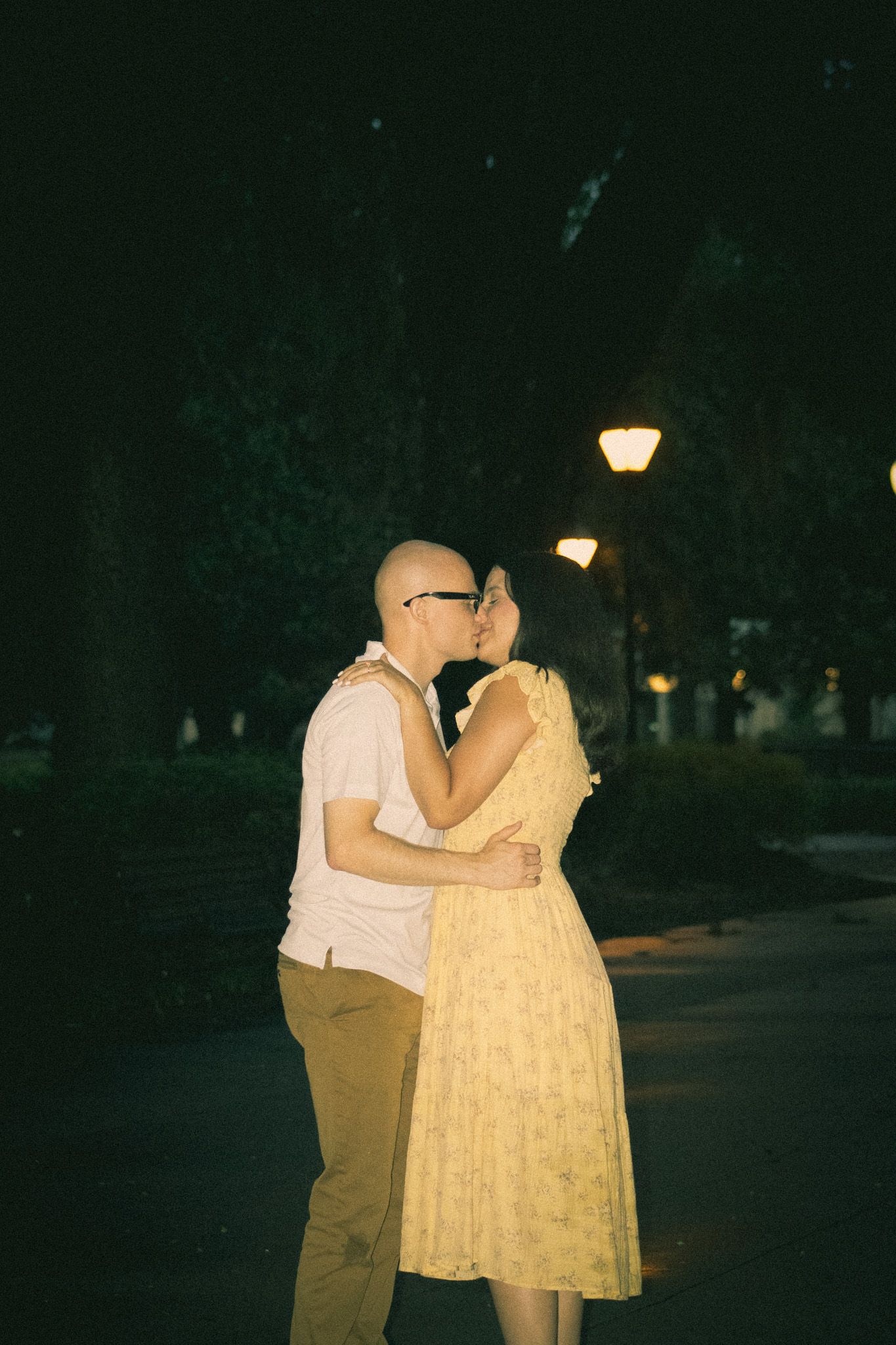 Couple shares an intimate moment in front of illuminated lamp posts at night.