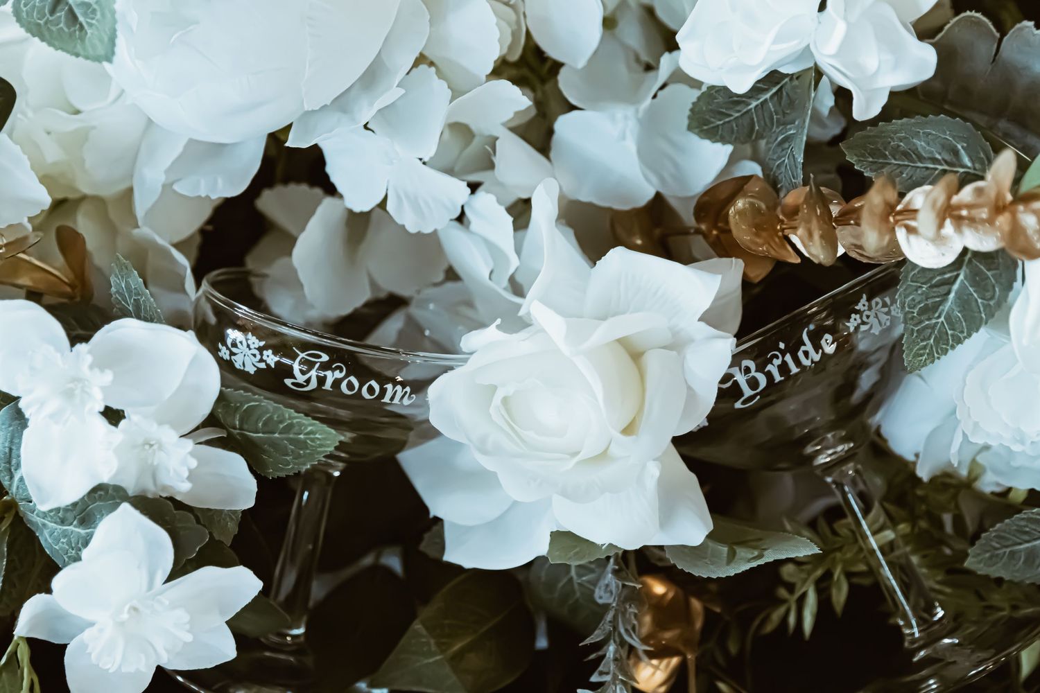 Elegant wedding glasses labeled Bride and Groom surrounded by white roses and floral arrangements.