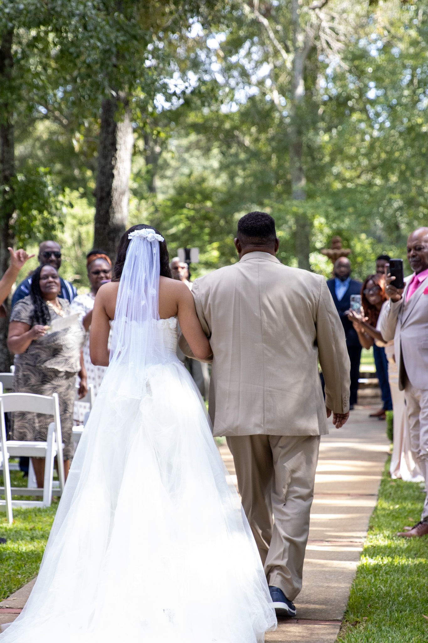 Couple walks down outdoor aisle after wedding ceremony with guests watching.