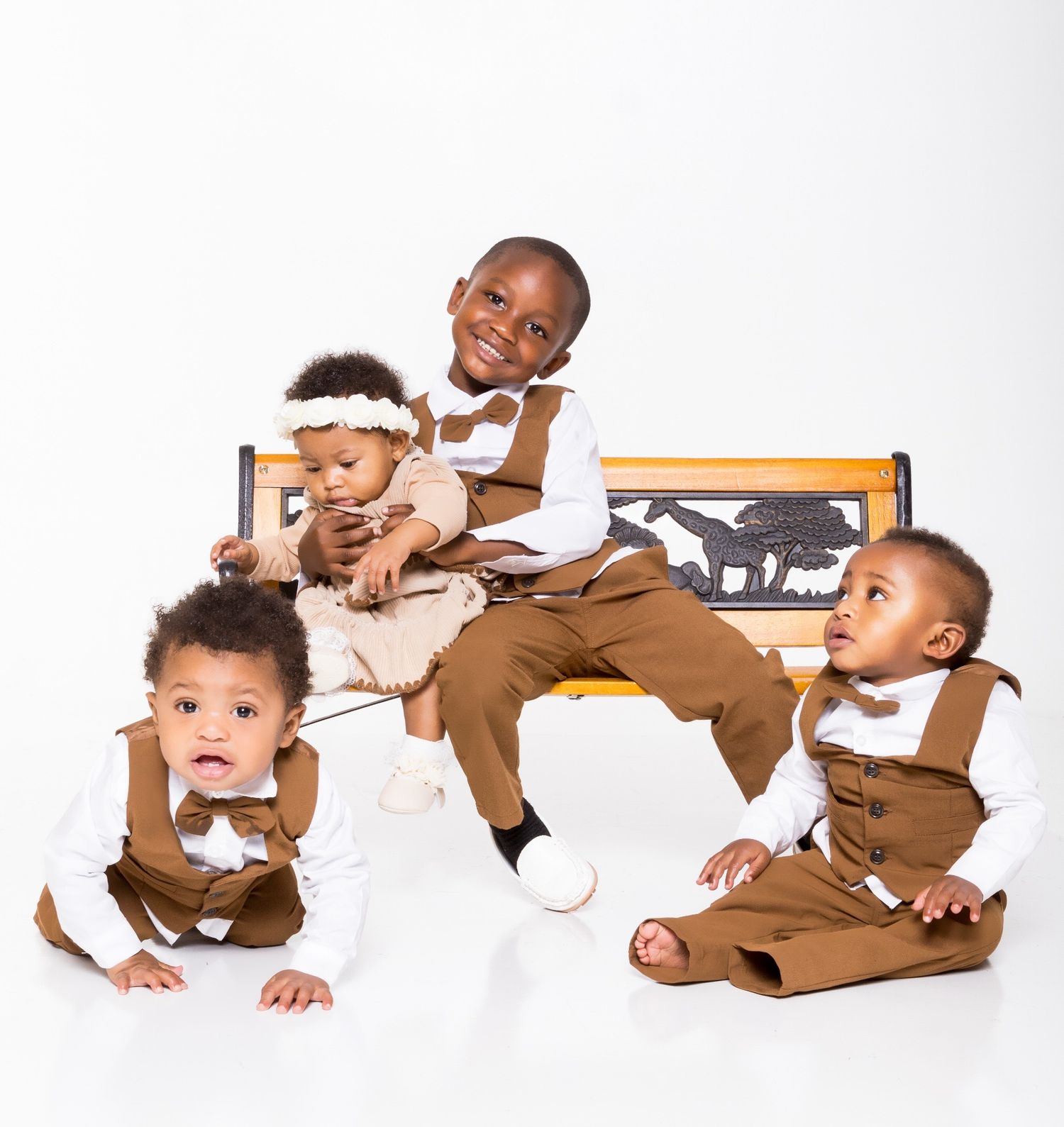 Four young children in coordinating brown and white outfits pose together near a decorative bench in a studio.